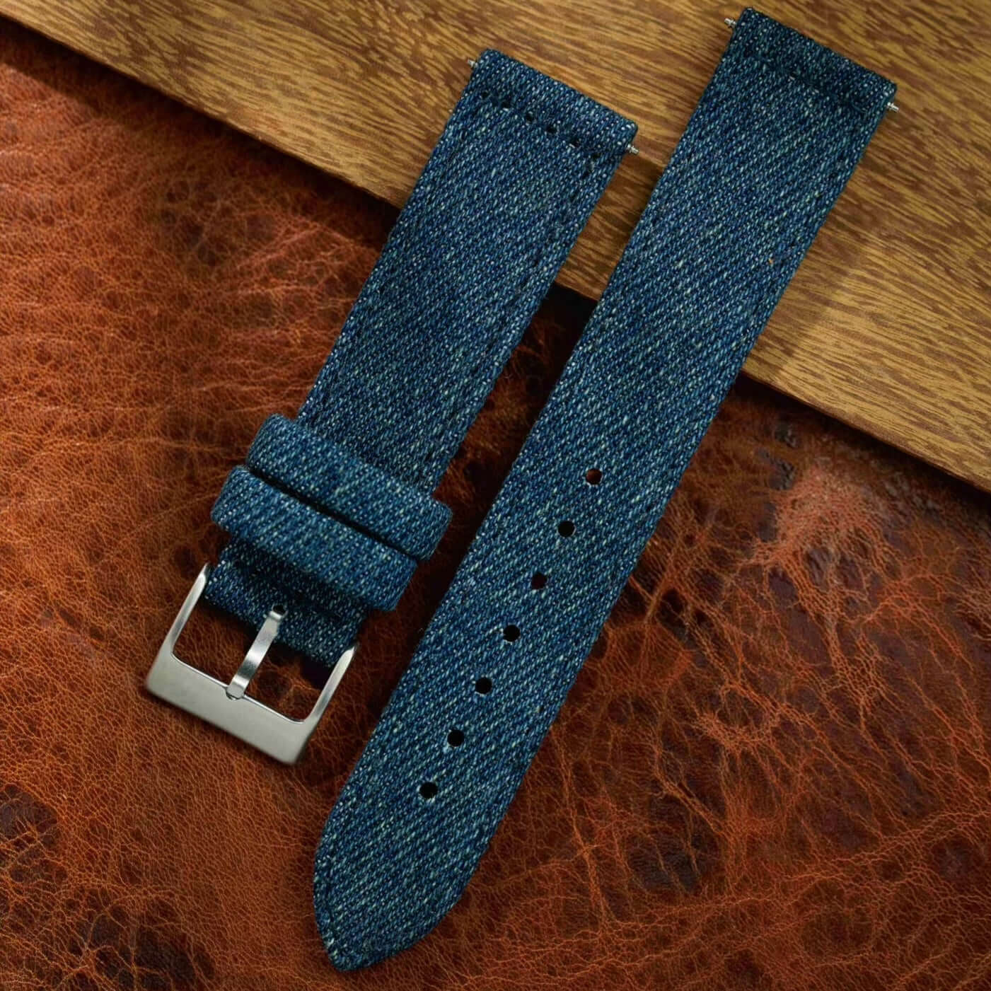 Jeans Uhrenarmband aus japanischem Denim mit strukturierter Optik, gefüttert mit schwarzem Kalbleder, auf braunem Hintergrund.