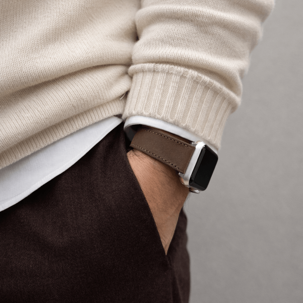 Mountain Apple Watch Lederarmband – Dunkelbraun am Handgelenk eines Mannes, kombiniert mit einem cremefarbenen Pullover und braunen Hosen.