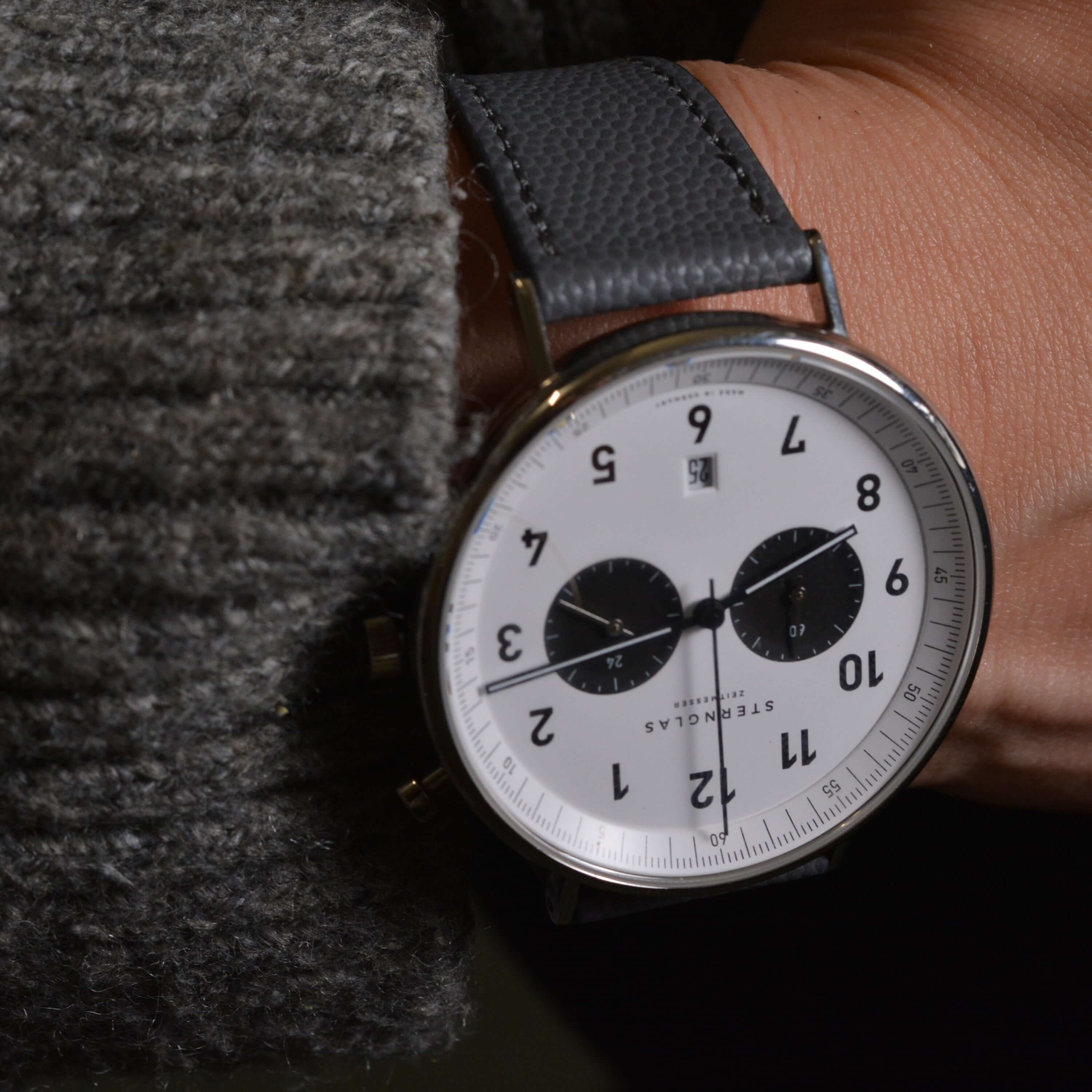 Stylish watch with a black leather strap on wrist, featuring a white dial with black numerals and two subdials, elegant and modern design.