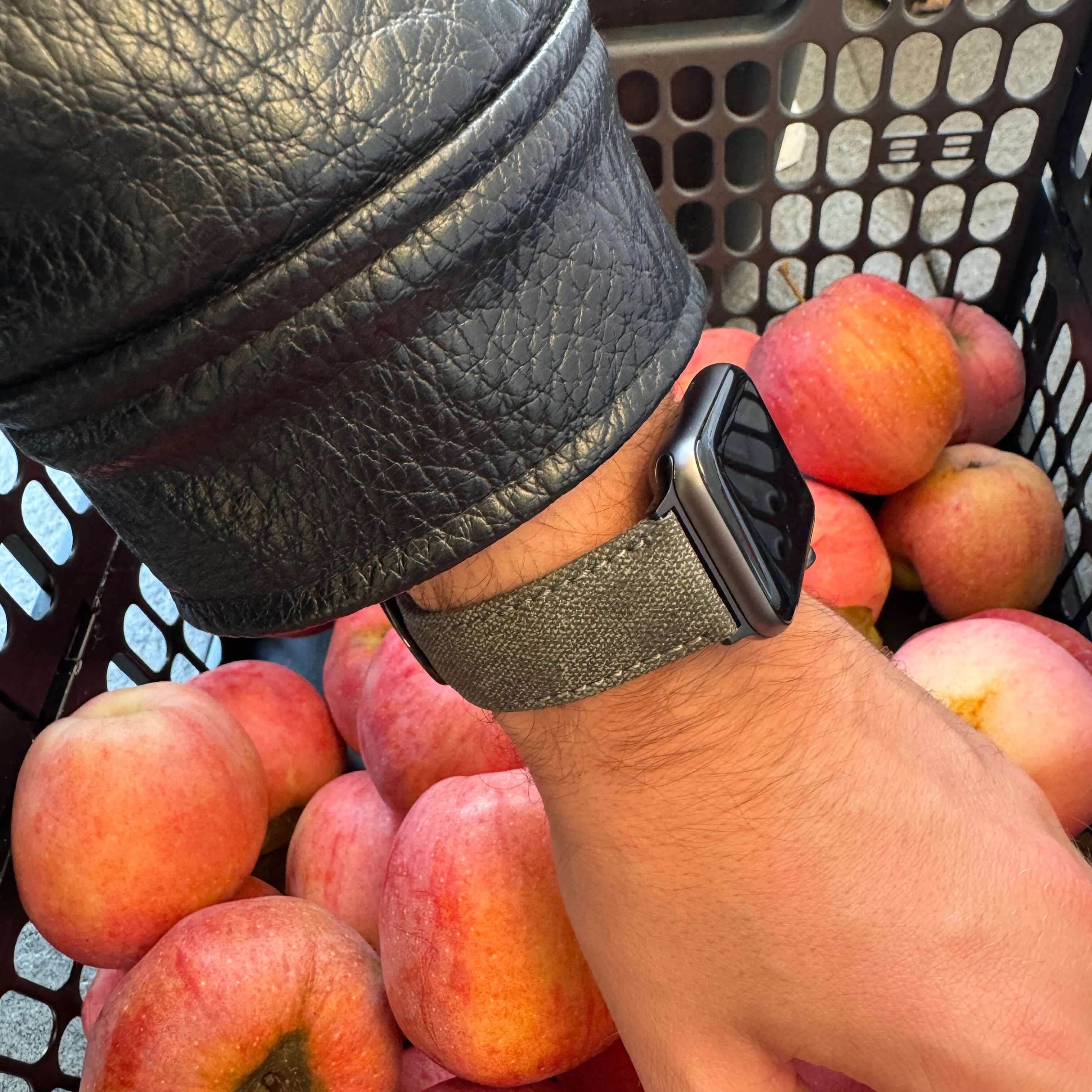 Graues Canvas Apple Watch Band Baumwolle an einem Handgelenk, umgeben von roten Äpfeln, stilvoll und funktional für den Alltag.