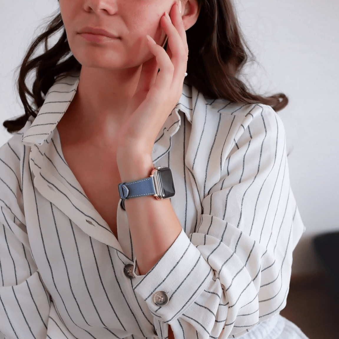 Frau trägt Hellblau kurzes Apple Watch Armband- Biarritz im modernen Design, passend zu ihrer gestreiften Bluse. Elegantes Accessoire am Handgelenk.