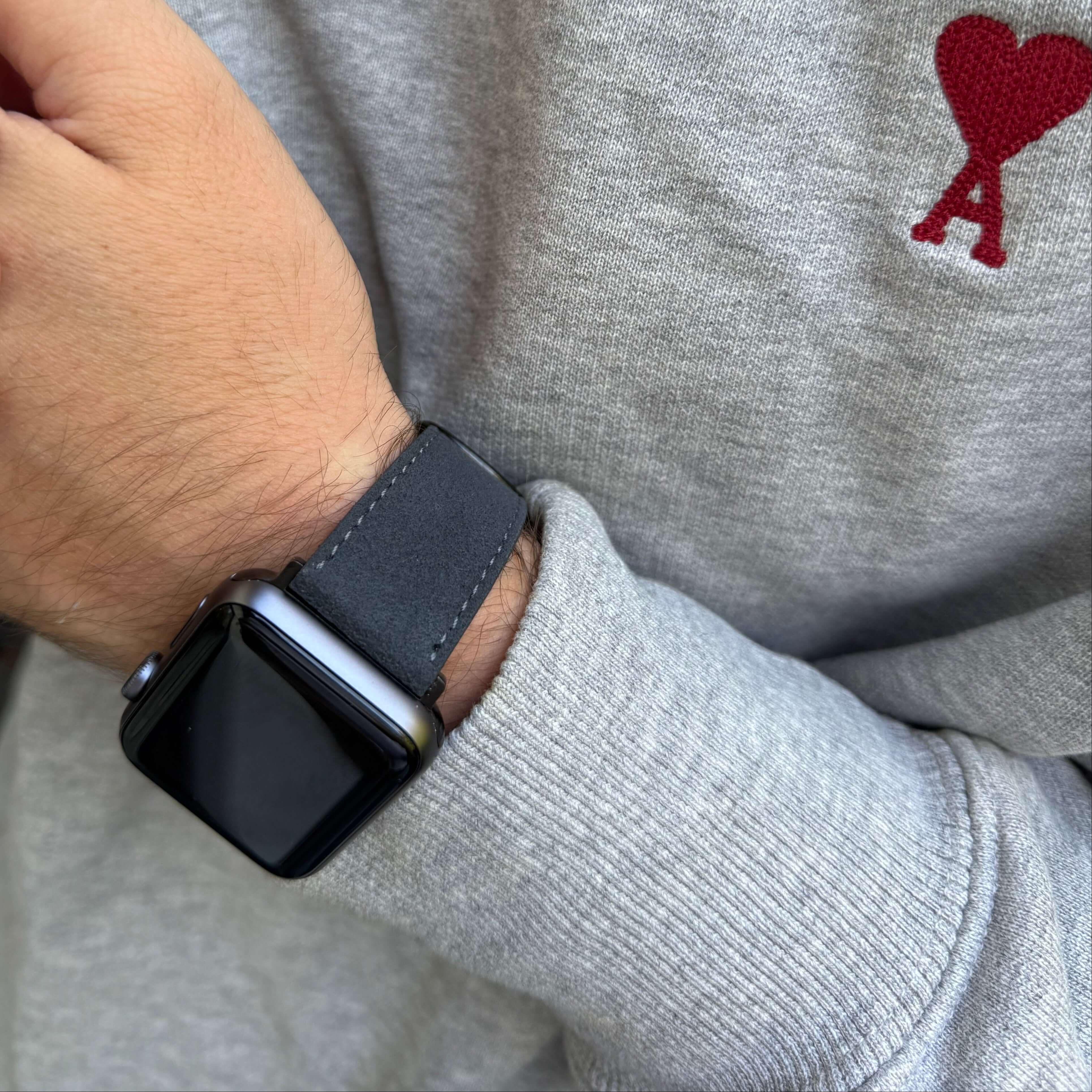 Stilvolles Alcantara Apple Watch Armband aus hochwertigem Stoff, getragen von einer Person in grauem Pullover mit Herzmotiv.