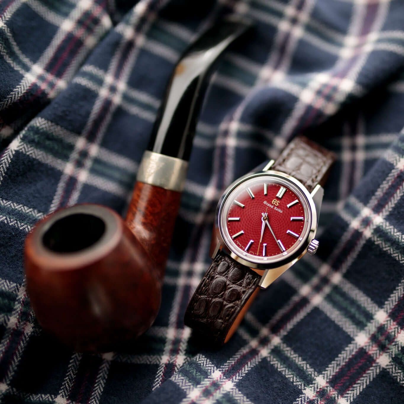 Luxuriöse Armbanduhr mit New Orleans Alligator Uhrenarmband auf kariertem Tuch neben Vintage-Pfeife