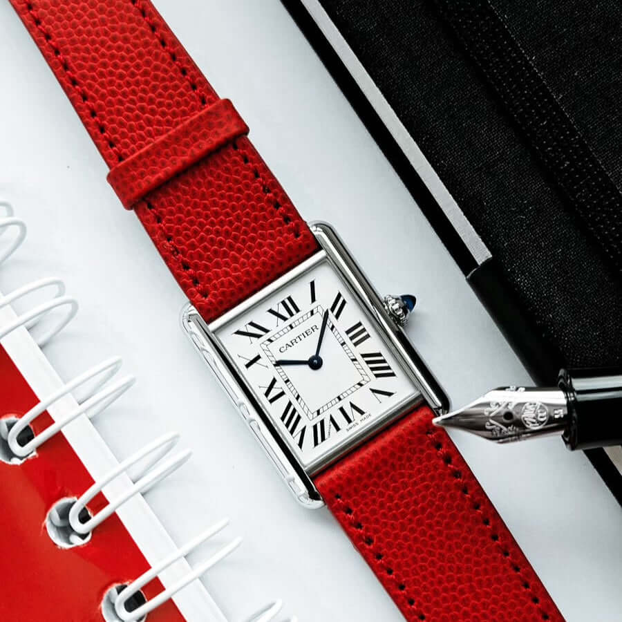 Luxurious watch with red Kaviarleder strap featuring Roman numerals, placed next to a notebook and pen.