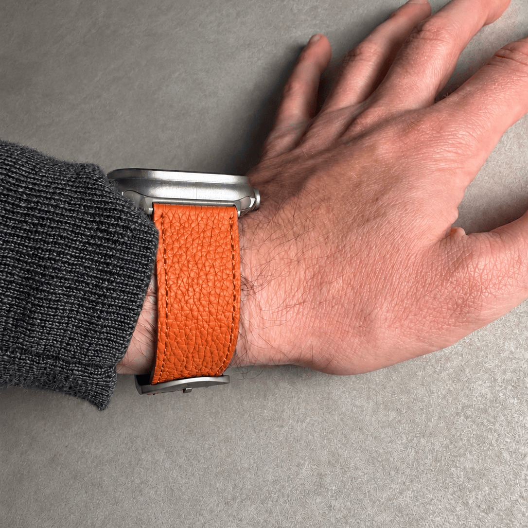 Oranges Lederarmband für Apple Watch aus Togoleder am Handgelenk mit silberner Uhr.
