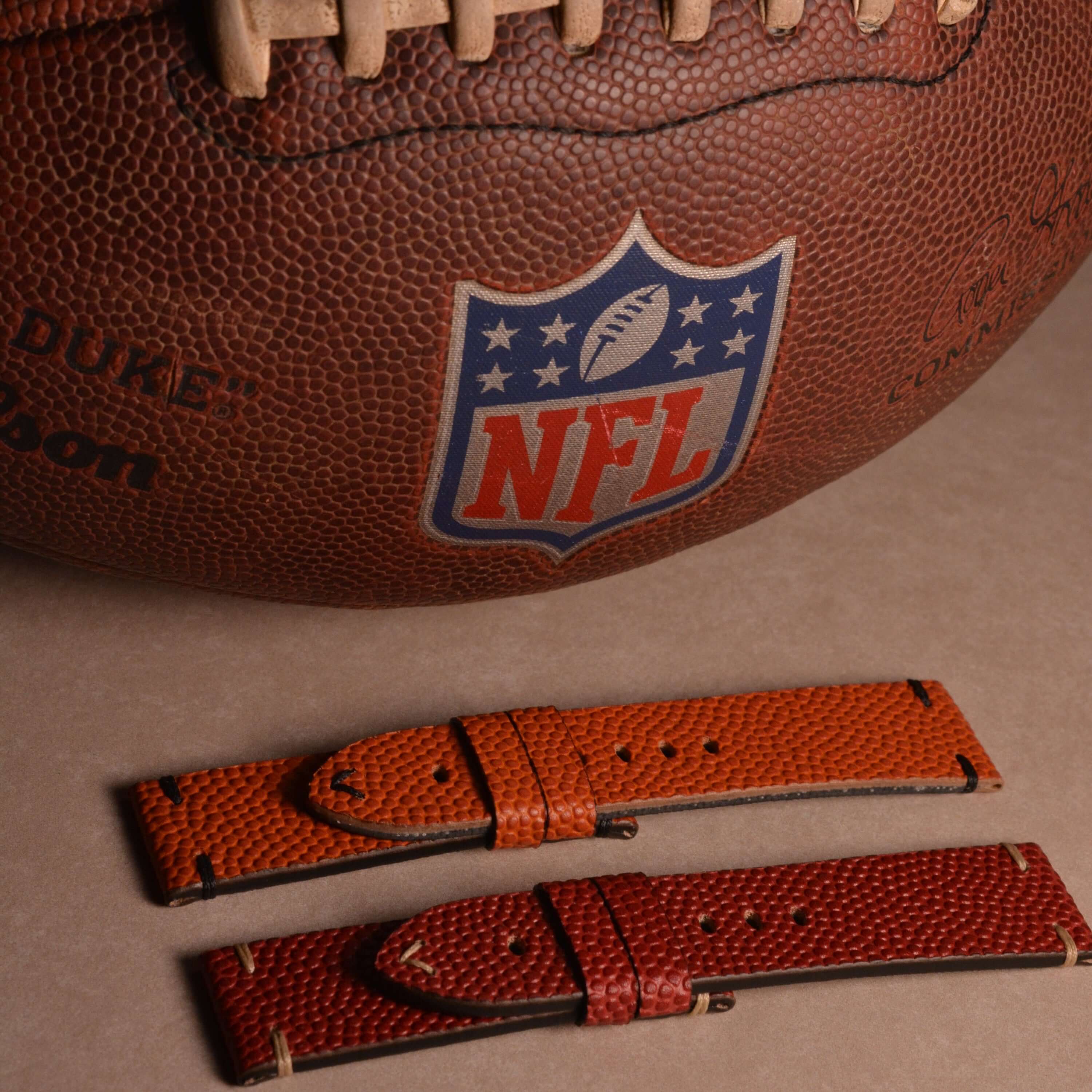Courtside – Uhrenarmband Handgefertigt aus original Horween Basketballleder neben einem NFL-Ball auf braunem Hintergrund