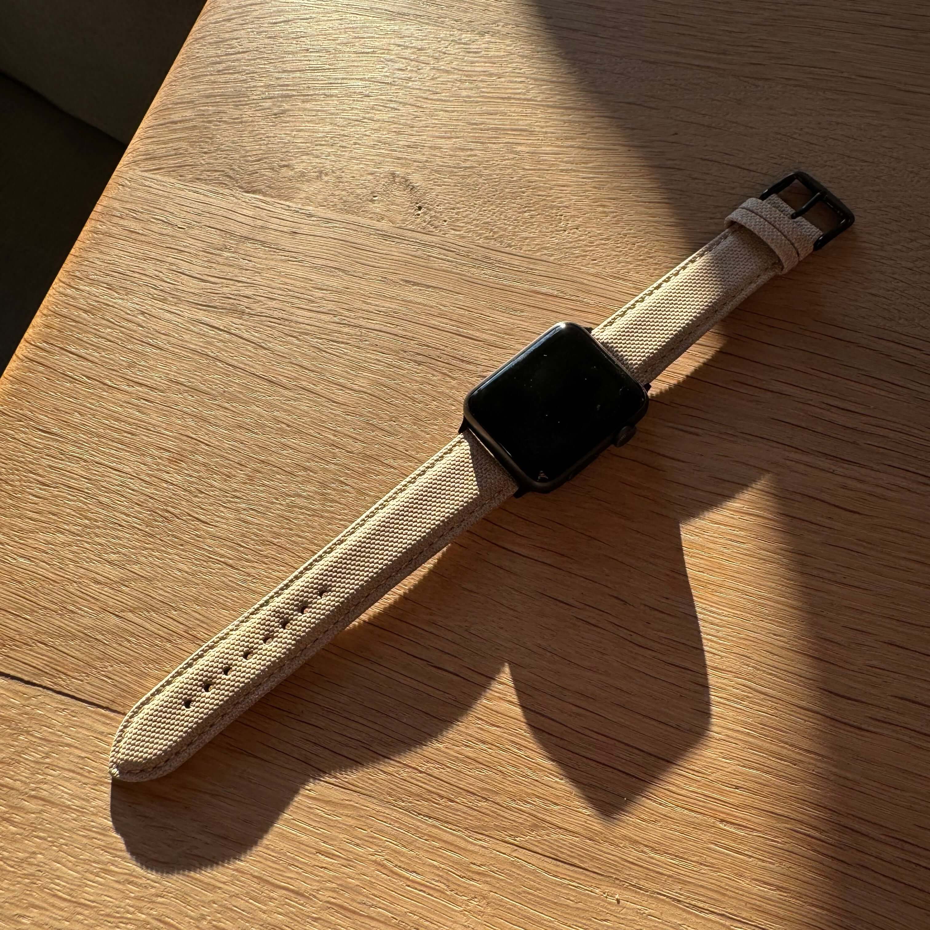Beiges Apple Watch Band Baumwolle auf einem hölzernen Tisch, zeitloses Design, wasserabweisend, geeignet für Alltag und Business.