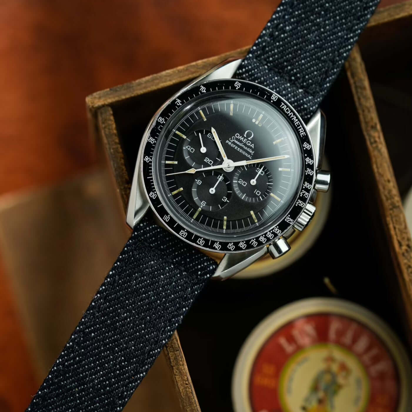 Luxus-Armbanduhr mit Jeans Uhrenarmband aus japanischem Denim in schwarzem Farbton, präsentiert auf einer Holzkiste.