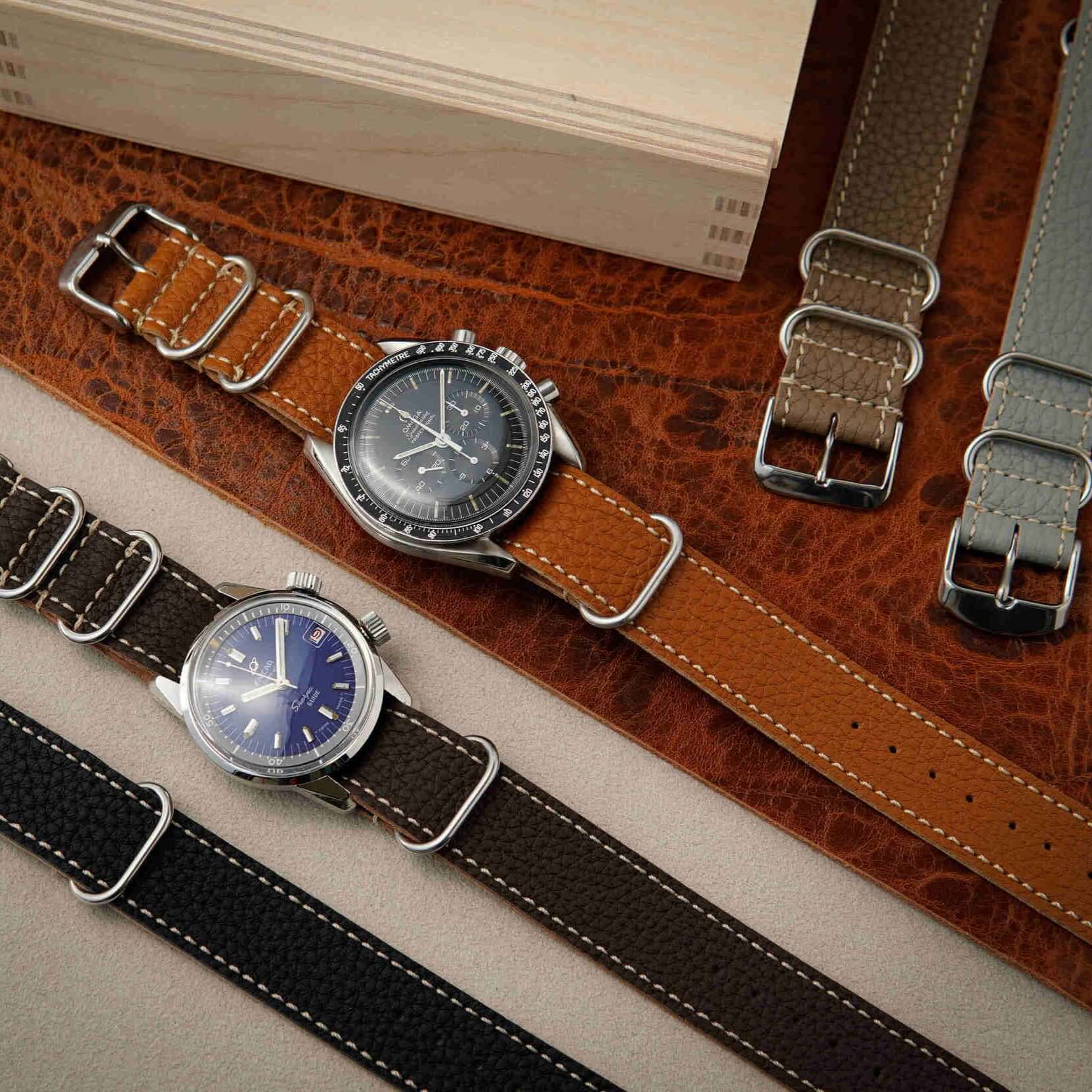Zwei Uhren mit Nato leder uhrenarmband herren in braun und schwarz, kombiniert auf einem Untergrund.