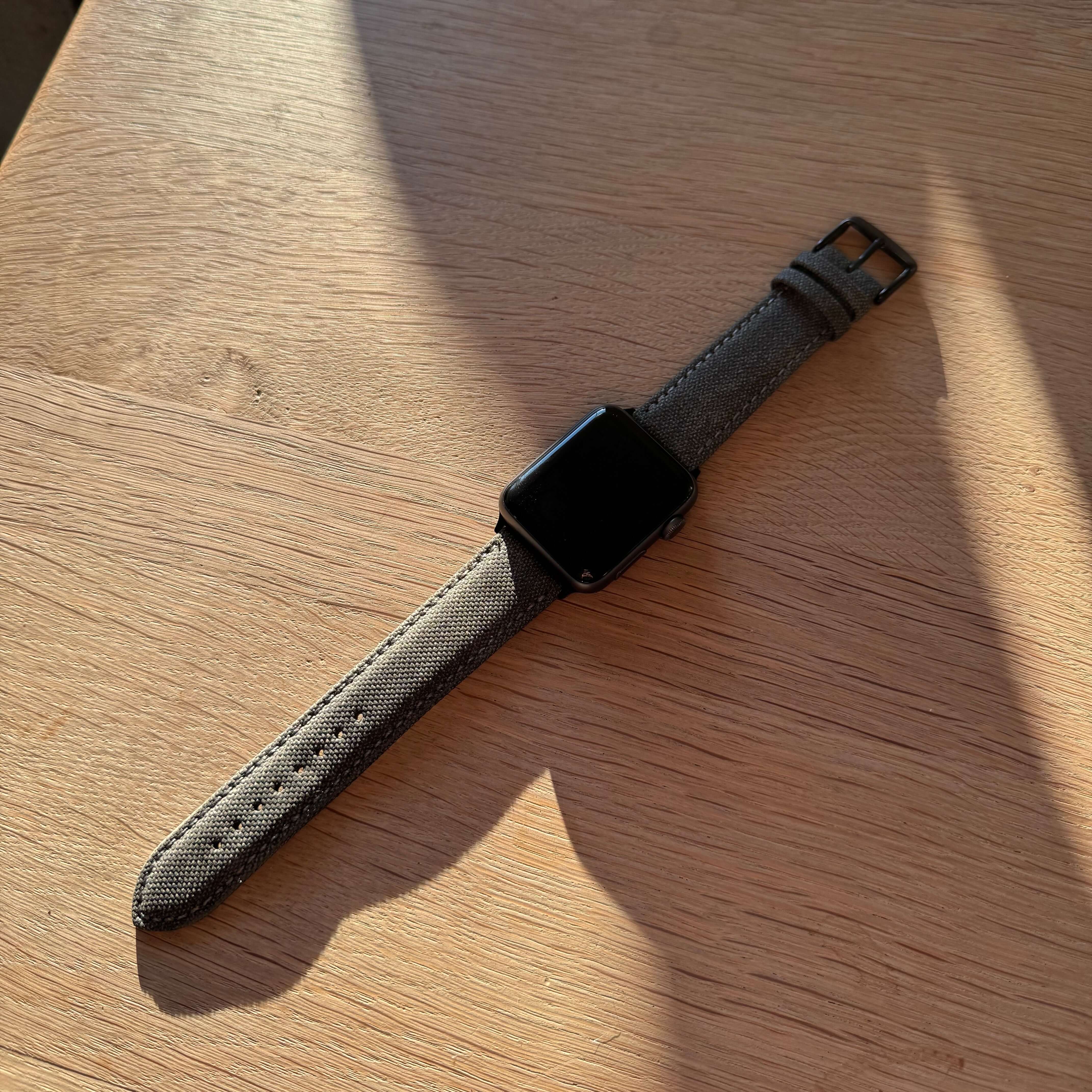 Graues Canvas Apple Watch Band Baumwolle auf Holzuntergrund, robust und stilvoll, vegan und wasserabweisend, 22 mm Breite.