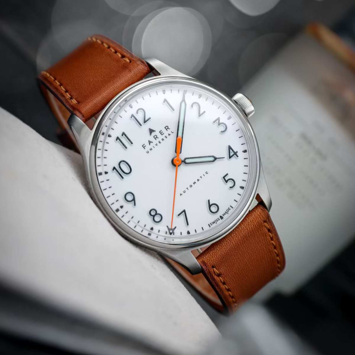 Eine Uhr mit silbernem Gehäuse und weißem Zifferblatt, gehalten an einem uhrenarmband leder in Braun. Das Armband verleiht der Uhr einen modernen und eleganten Look.