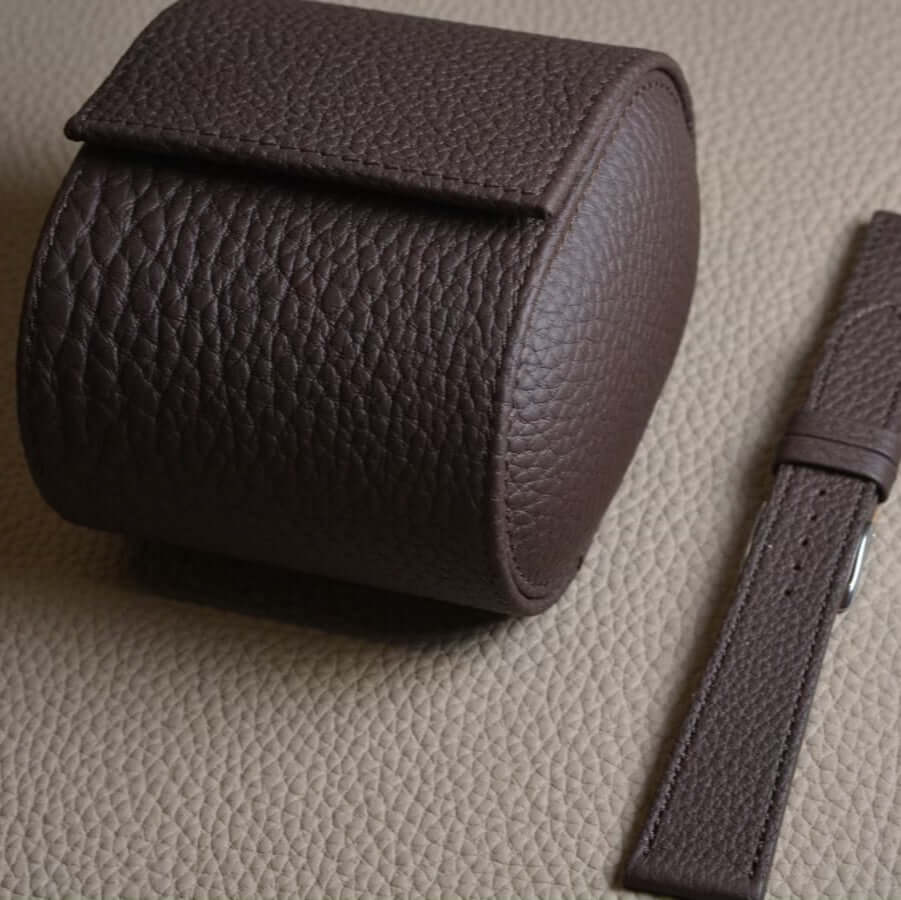 Brown Togo leather watch roll and Deauville strap set on textured surface.