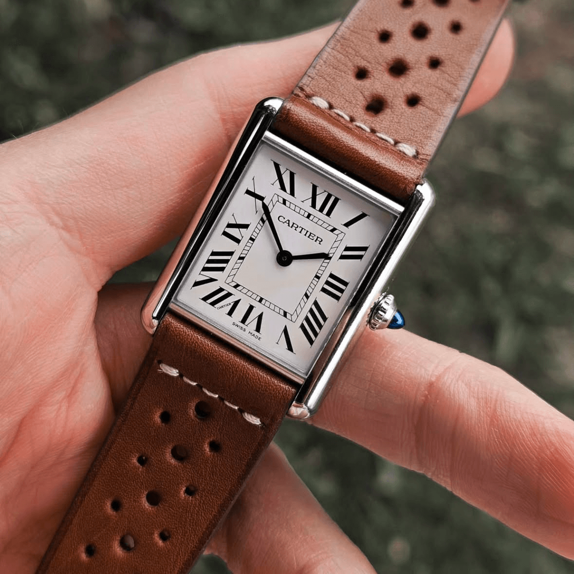 Paris Racing – Armband aus Barenia-Leder mit sportlicher Lochprägung an einer klassischen Armbanduhr, präsentiert auf einer Hand.