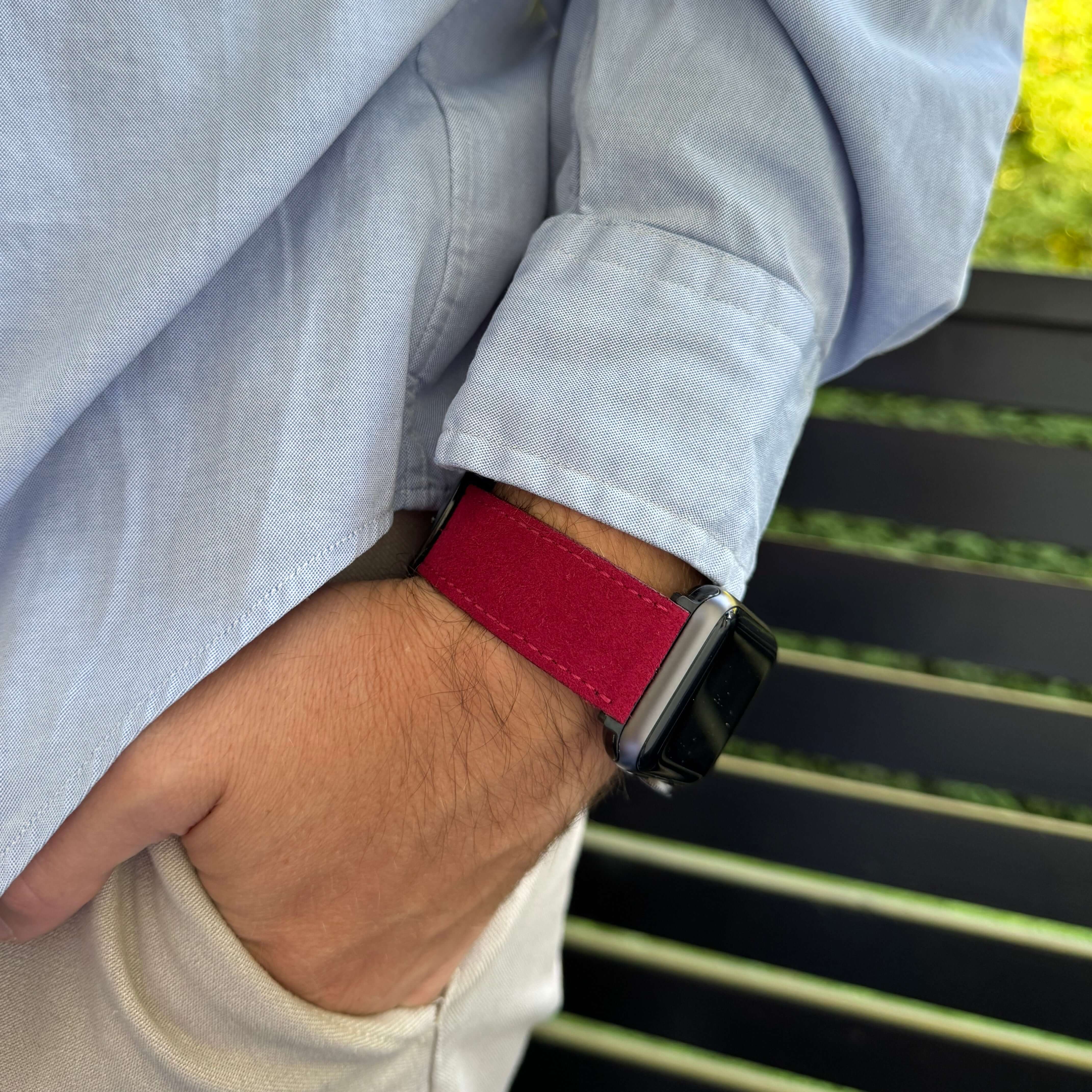 Person trägt Apple Watch mit rotem Alcantara-Armband an einem sonnigen Tag, stilvolle Ergänzung für elegantes Outfit.