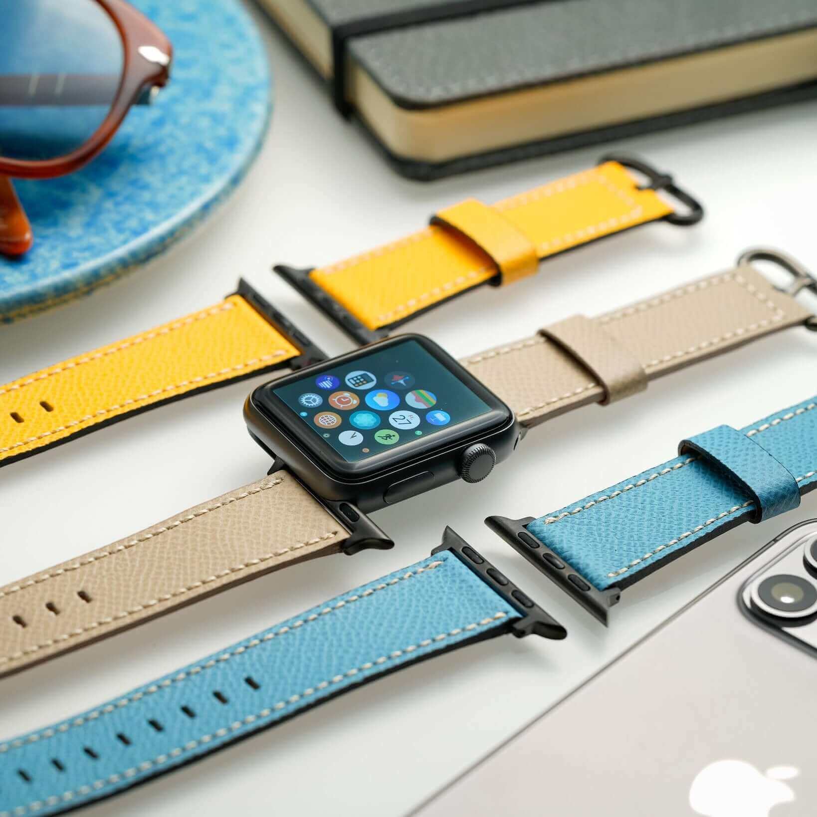 Luxuriöses Apple Watch Lederarmband in Hellblau, Beige und Gelb auf Schreibtisch, stilvolles Accessoire für Damen