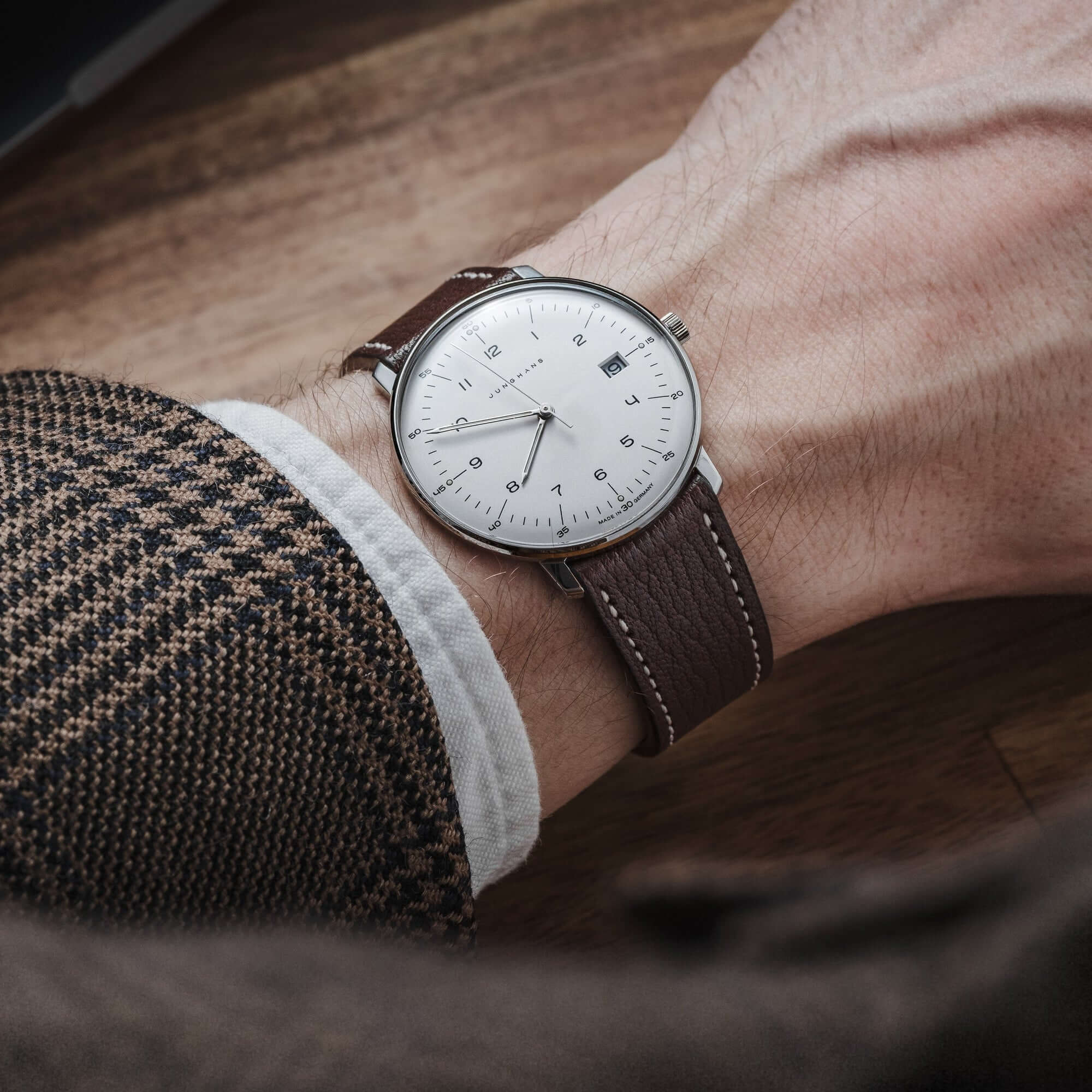 Mann mit Armbanduhr und Biarritz – Uhrenarmband aus französischem Ziegenleder in Dunkelbraun, getragen auf einem Holztisch.