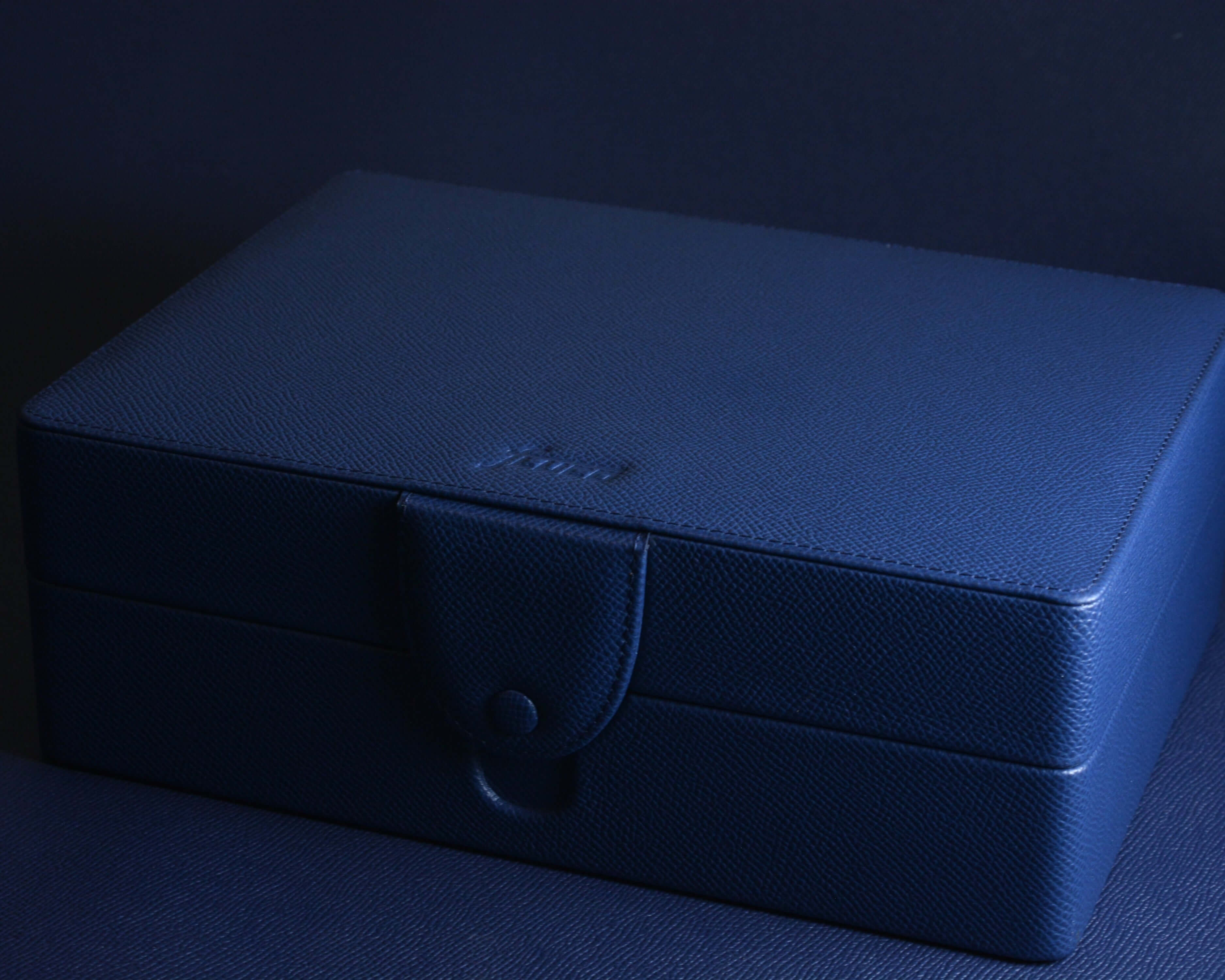 Luxury blue jewelry box with textured finish on a dark background.