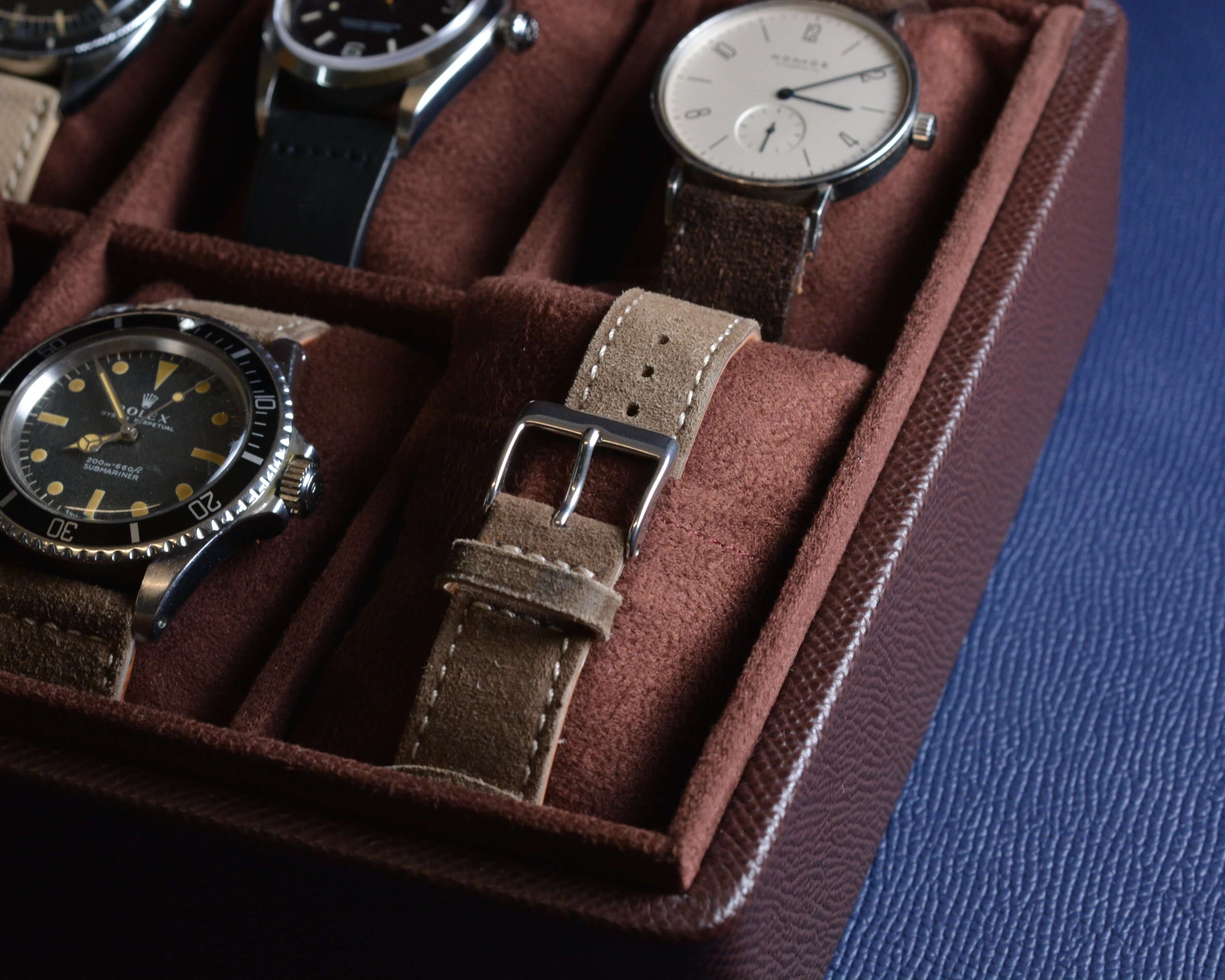 Close-up of luxury watches in a brown leather case displaying elegant timepieces with various strap designs.