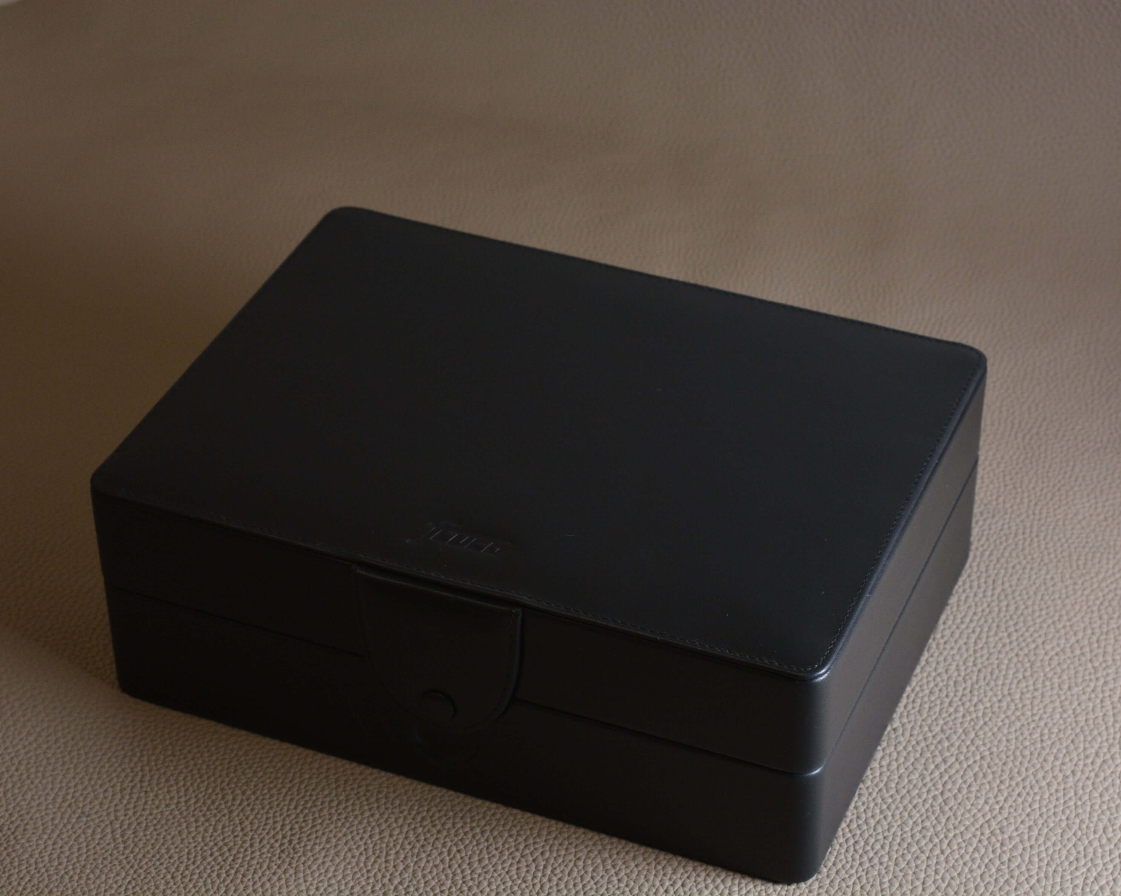Elegant closed black leather box on a beige surface.