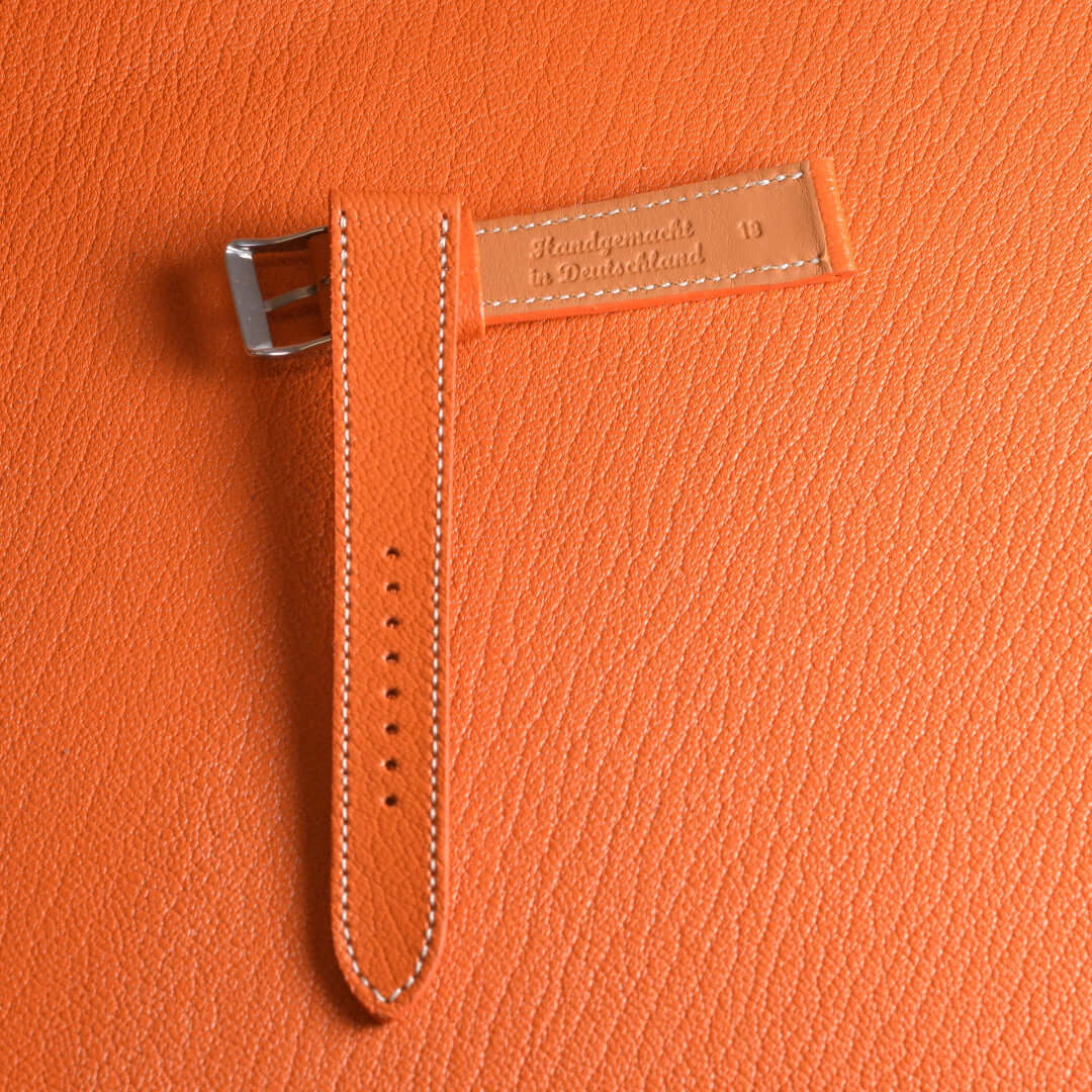 Orange Uhrenarmband aus Leder, handgefertigt in Deutschland, auf oranger Texturhintergrund liegend, Vintage Look.