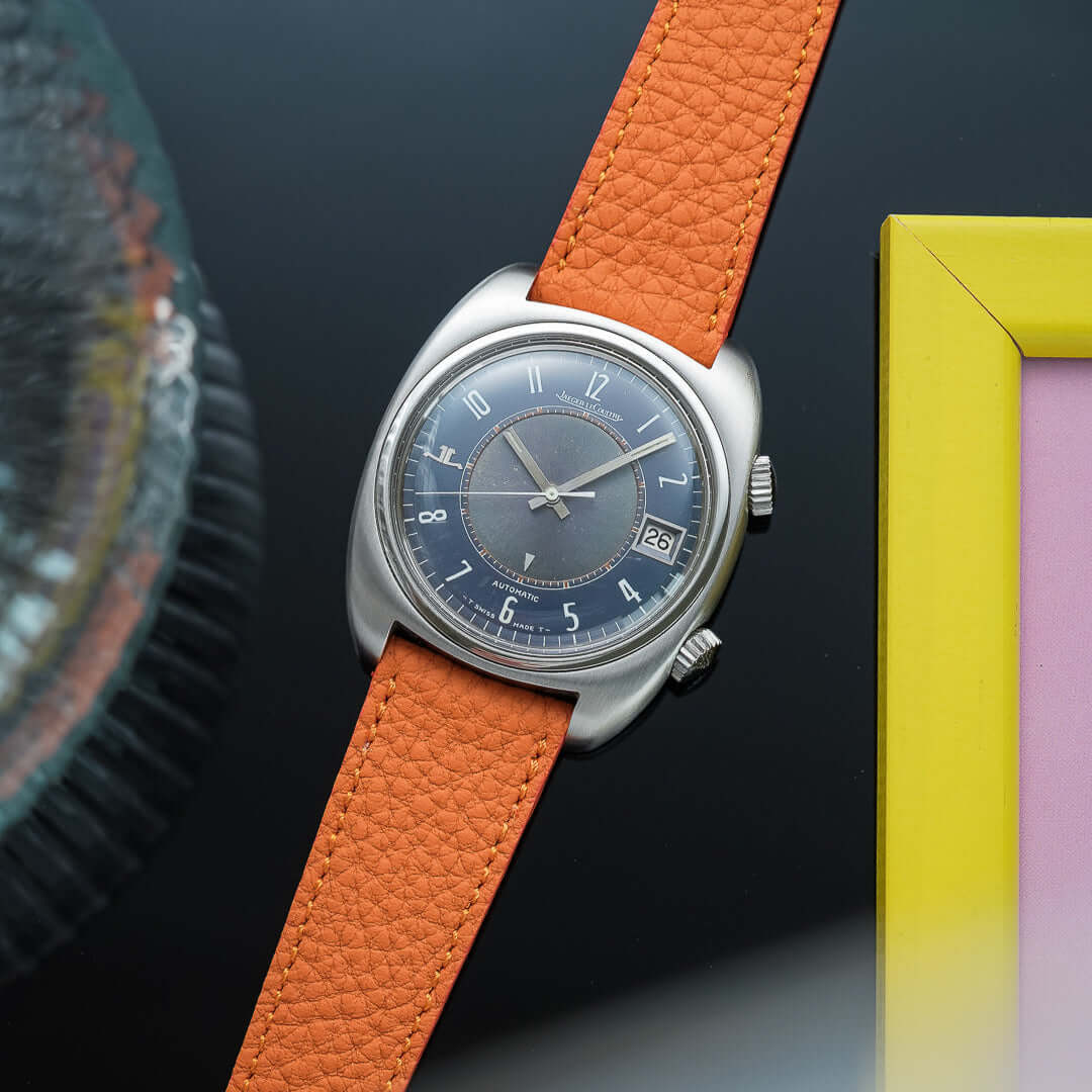 Luxurious watch featuring an orange Deauville Leder Uhrenarmband on a stylish dial set against an artistic background.