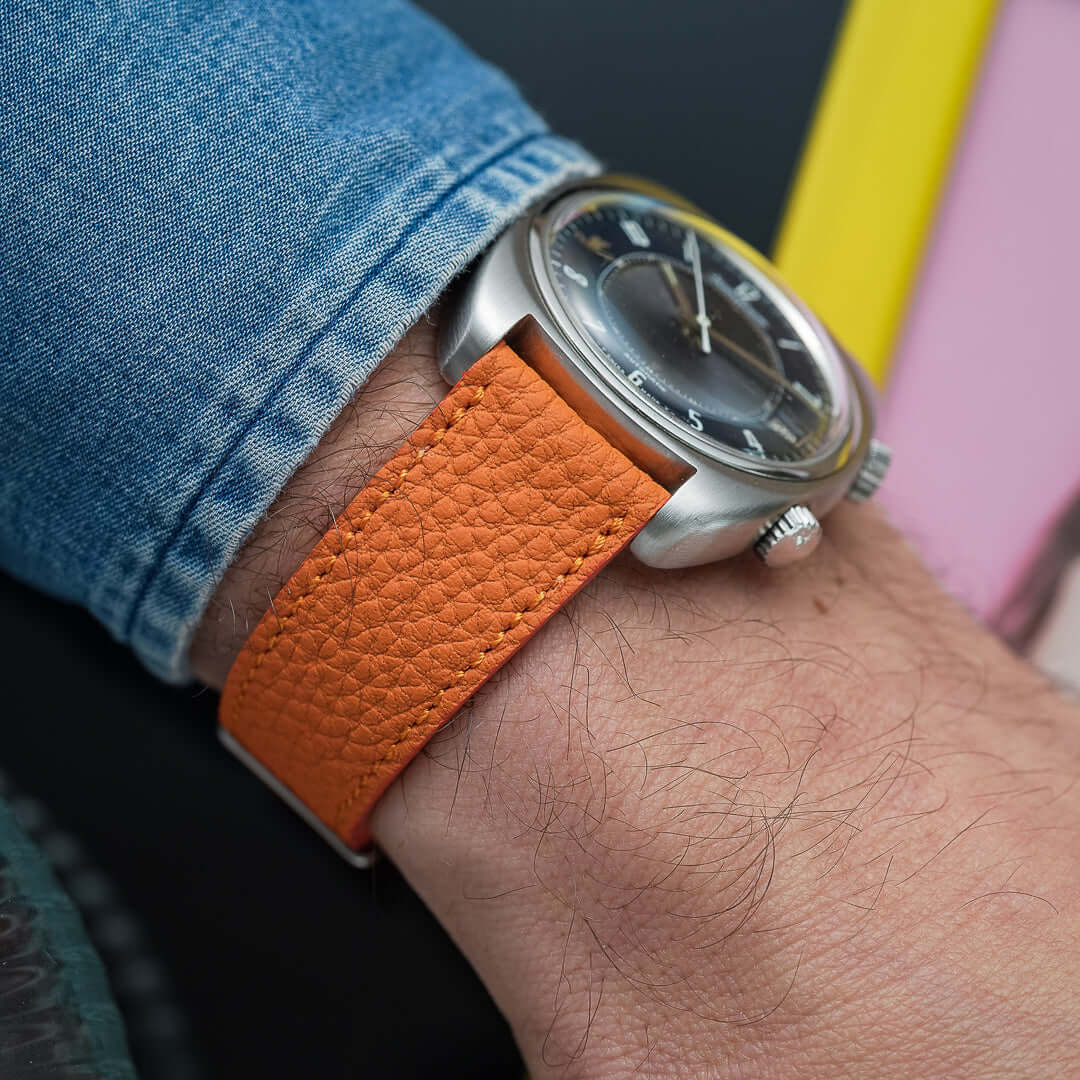 Deauville Leder Uhrenarmband mit orangefarbenem Togoleder, elegante Ton-in-Ton-Kantenfarbe, Edelstahlverschluss, auf Männerhand.