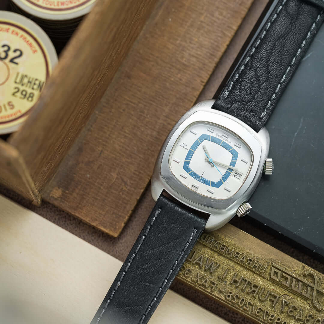 Close-up of a stylish watch with black leather strap on a wooden surface, showcasing modern design and craftsmanship.