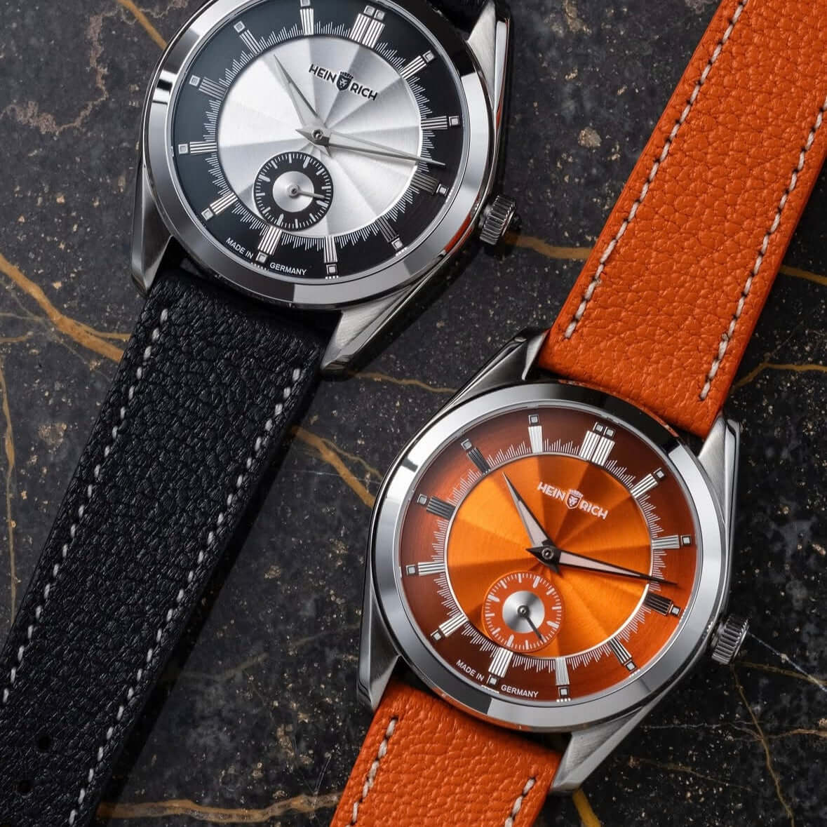 Zwei Uhren mit Biarritz Uhrenarmband Leder hochwertig in Schwarz und Orange auf Marmorhintergrund.