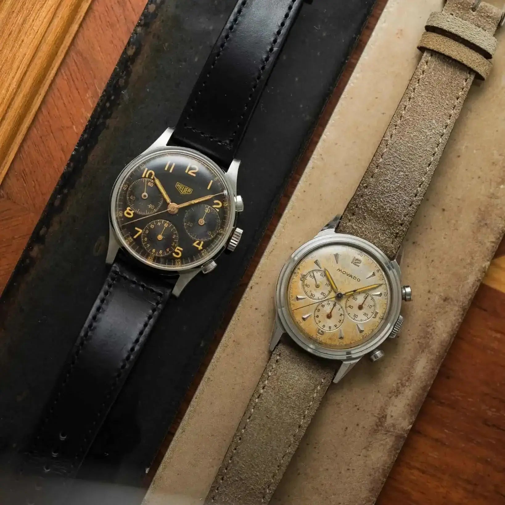 Zwei Vintage-Uhren mit Horween Chrom Excel Leder Uhrenarmband, eines in Schwarz und das andere in Beige, auf einer Holzoberfläche.