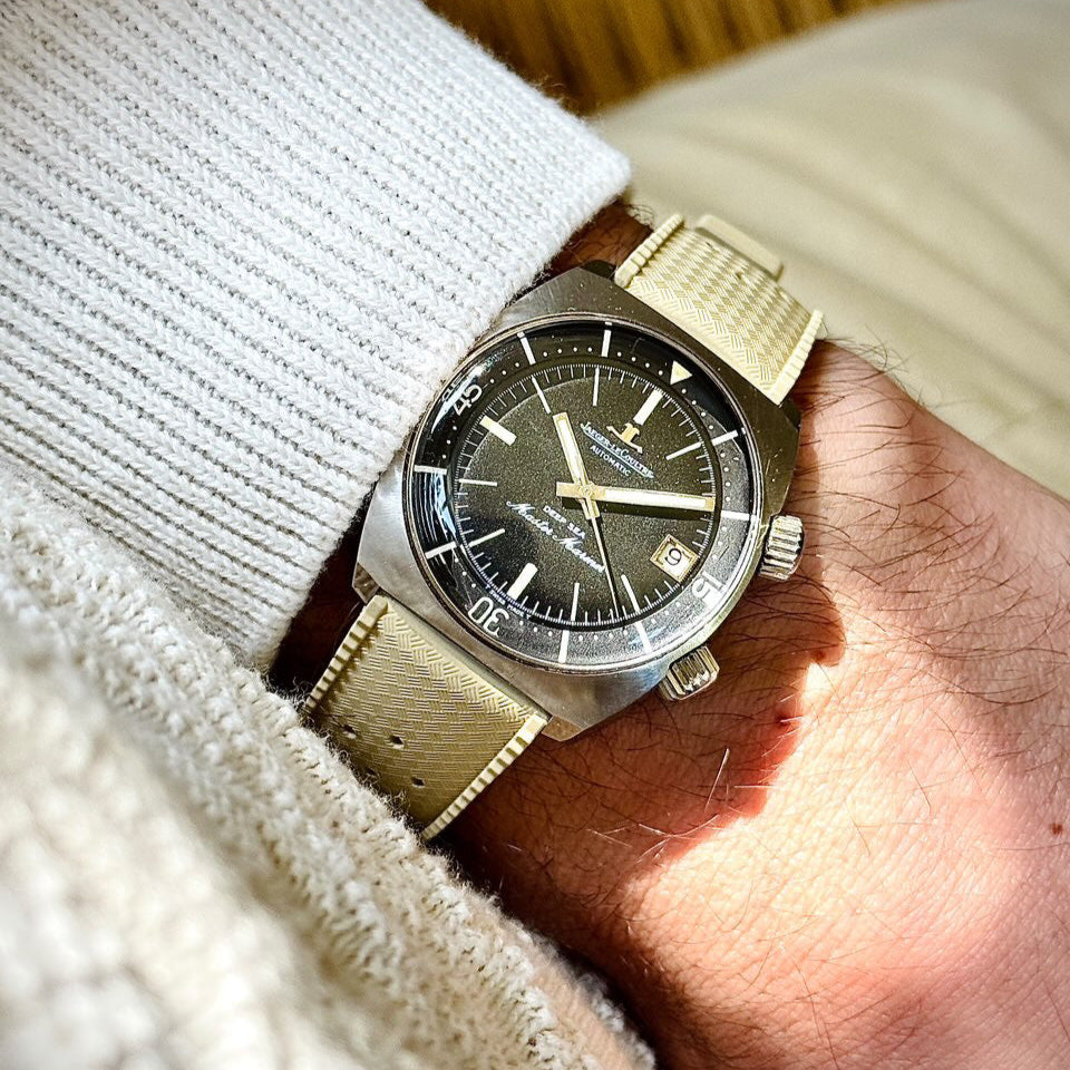 Vintage-style wristwatch on a man's arm with a beige leather strap and silver watch case, showcasing a dark dial with luminous markers.