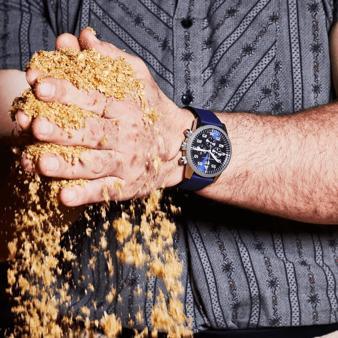 Mann mit wasserfestem Uhrenarmband Nautilus hält Getreide in den Händen, symbolisiert Kombination aus Stil und Funktionalität.
