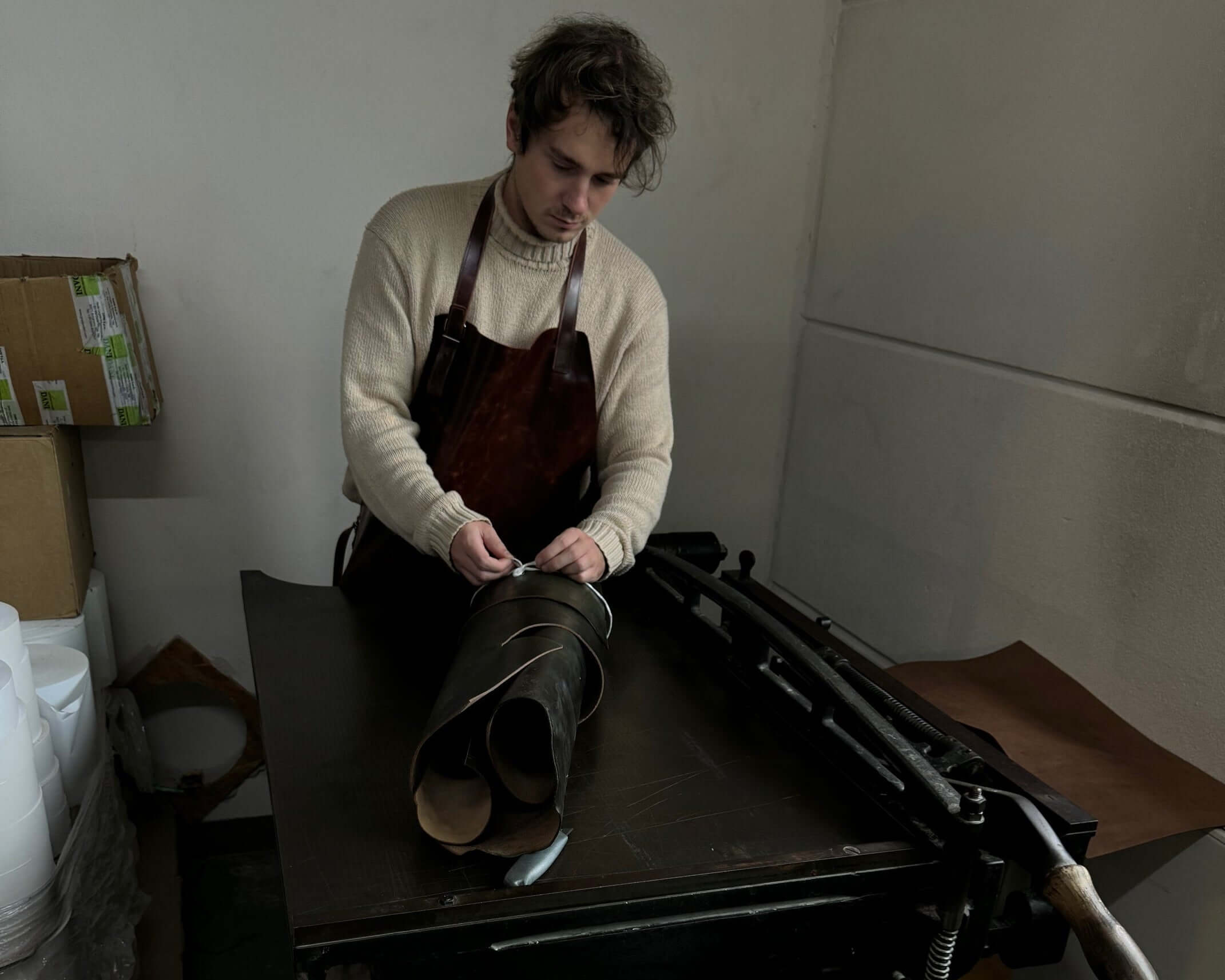 Man in apron crafting leather boots using traditional tools in workshop.