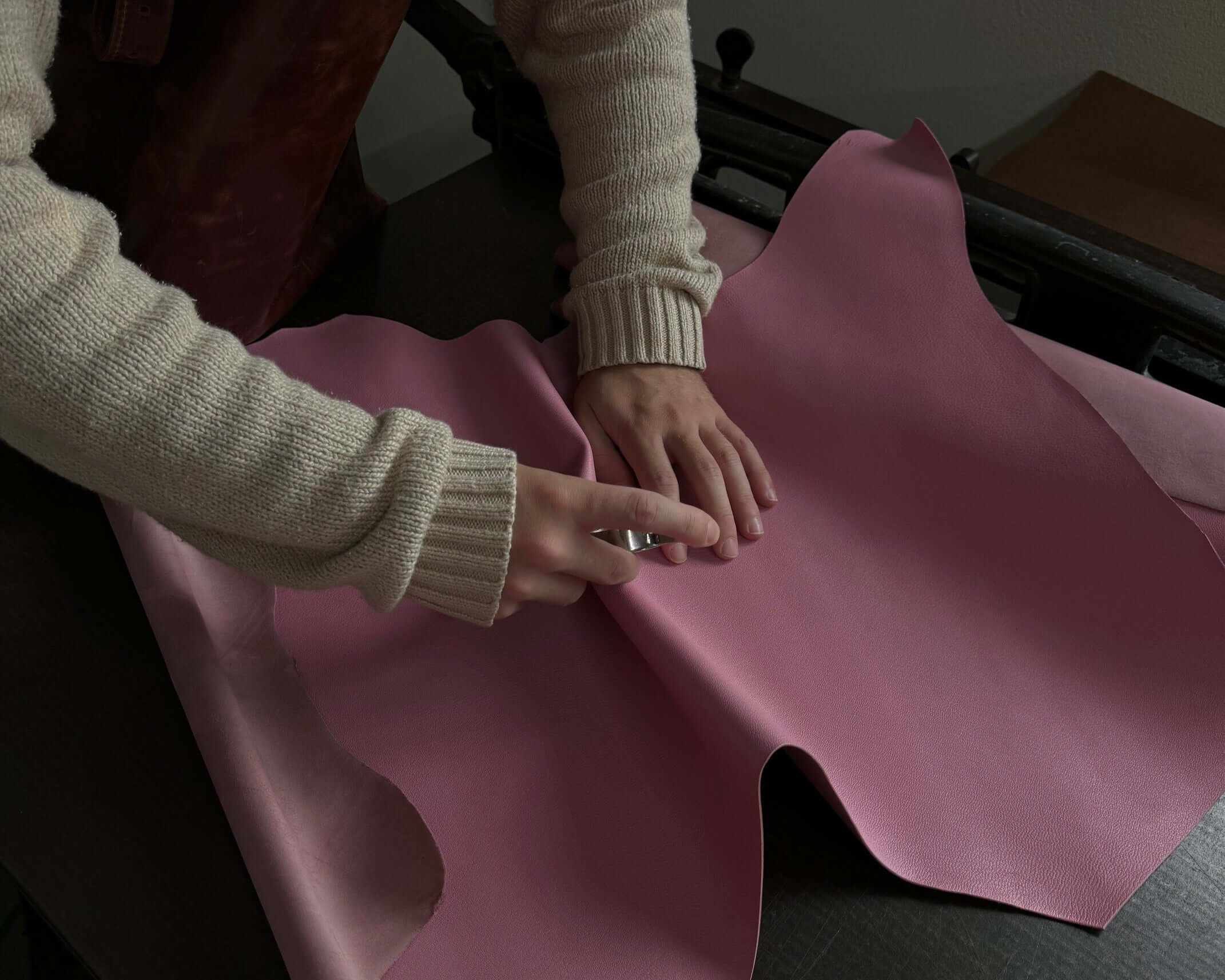 Person crafting with pink leather fabric on a dark work table, demonstrating leatherworking techniques and craftsmanship.