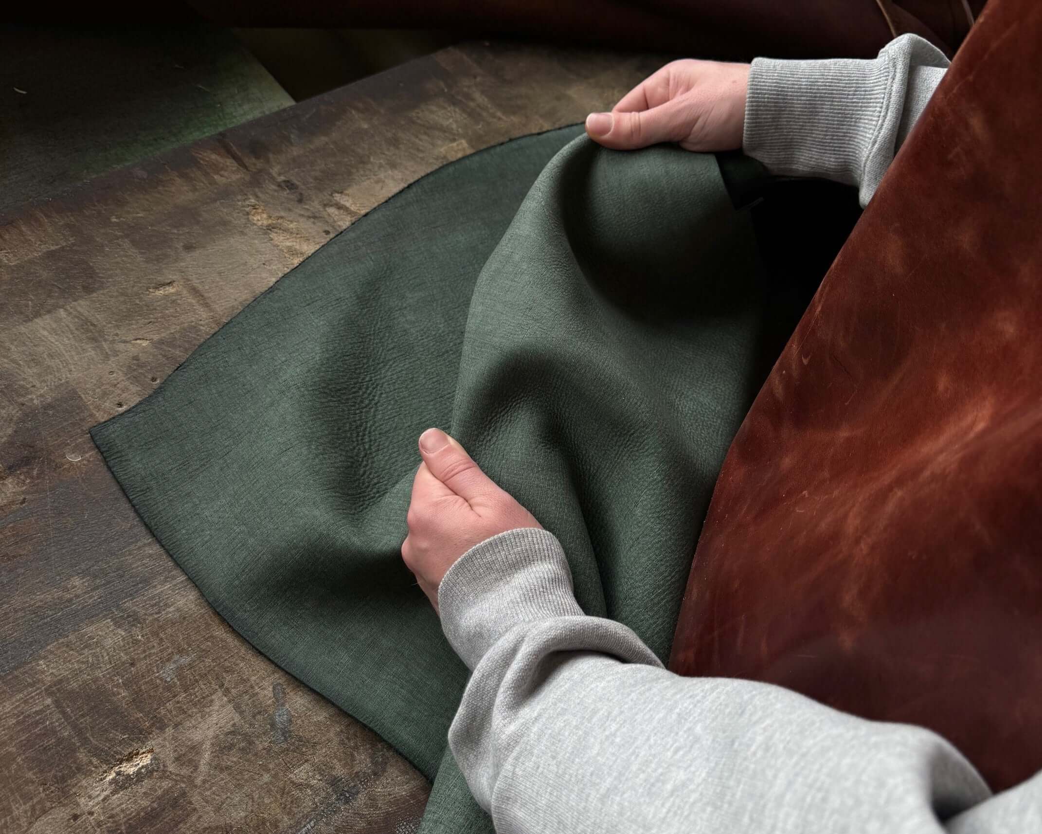 Person examining quality of dark green fabric on wooden table.