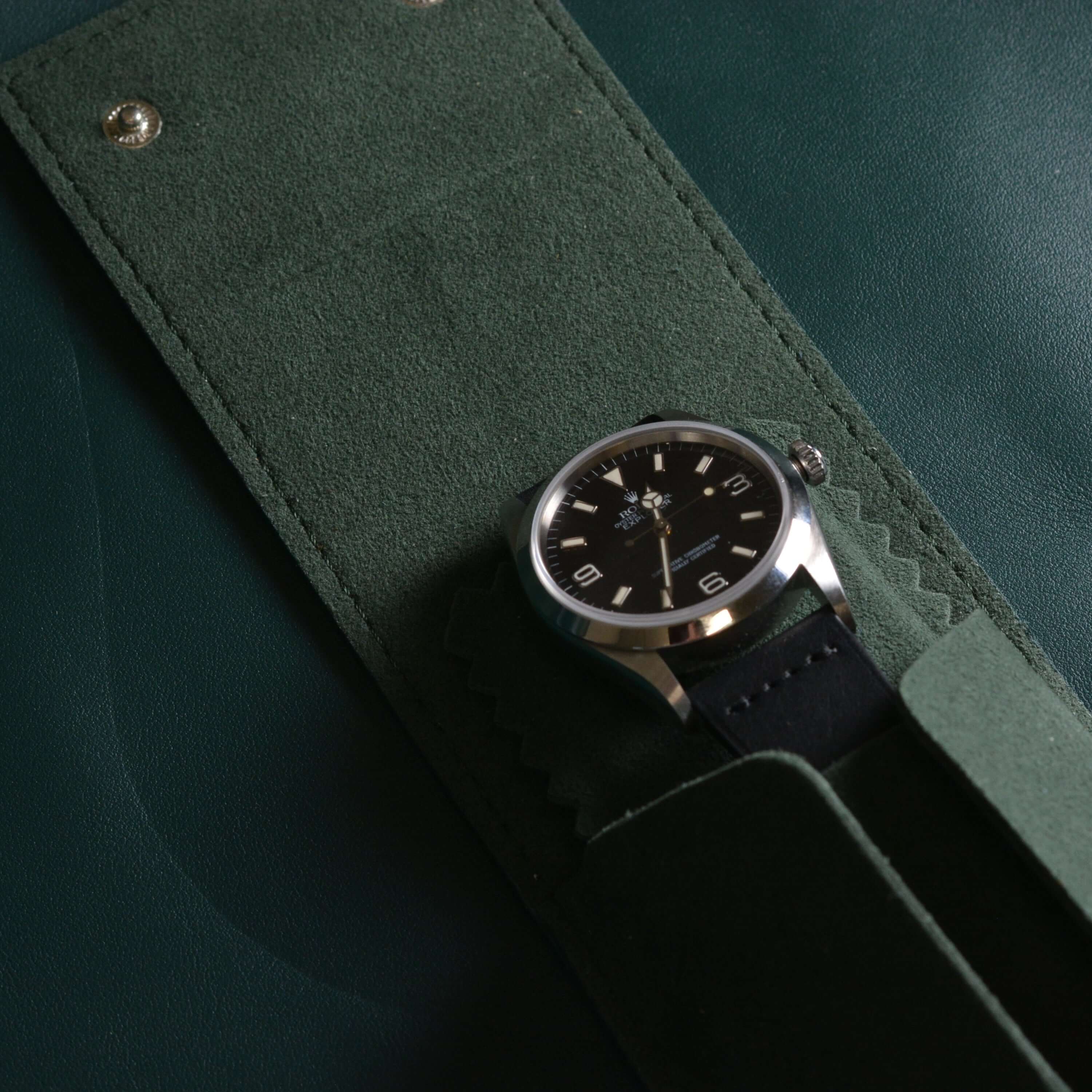 Offenes grünes Uhrenetui aus vegetabil gegerbtem Rindleder mit weichem Alcantara-Innenfutter, darin eine hochwertige Rolex Explorer mit schwarzem Ziffernblatt mit schwarzem Lederarmband – ideal für sichere Uhrenaufbewahrung auf Reisen.