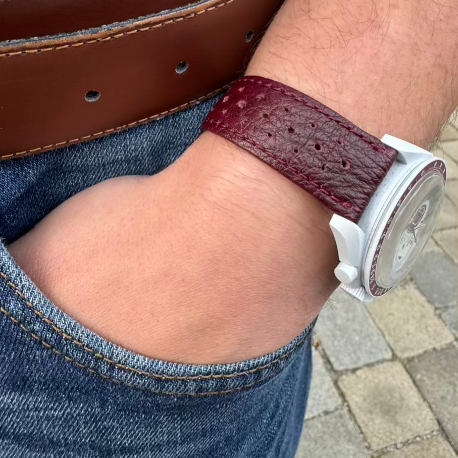 Uhrenarmband aus echtem Leder in Bordeaux von FLUCO – handgefertigt in Deutschland mit Kontrastnaht. Am Handgelenk einer Omega Swatch.