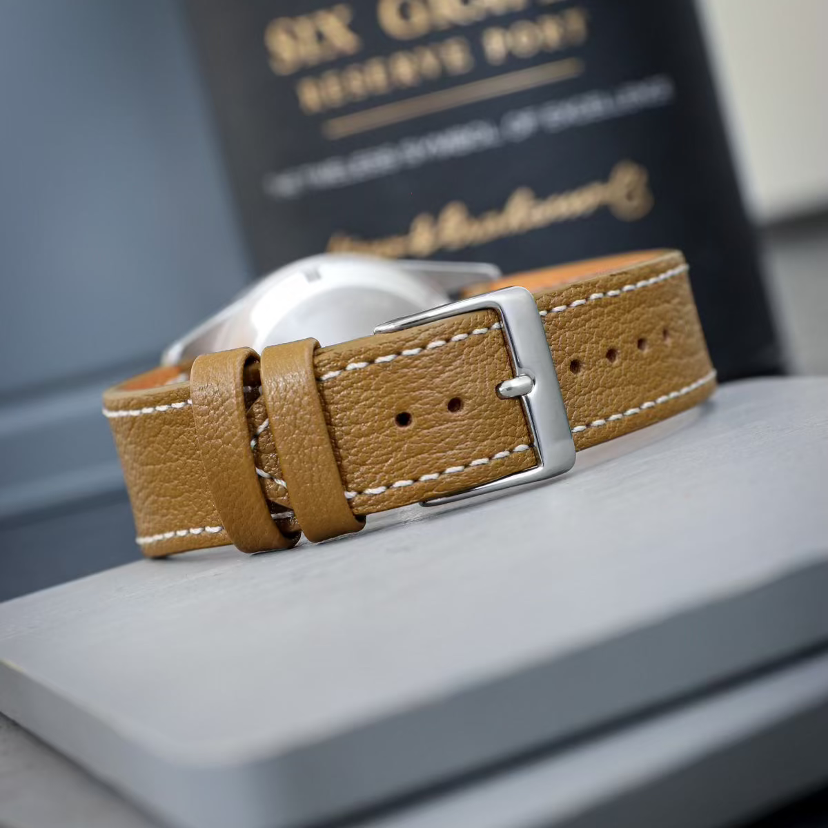Detailaufnahme eines braunen, kurz geschnittenen Uhrenarmbands aus Leder mit einer silbernen Schließe. Das kurzes Uhrenarmband hat eine natürliche Maserung und ist auf einem grauen Untergrund platziert.