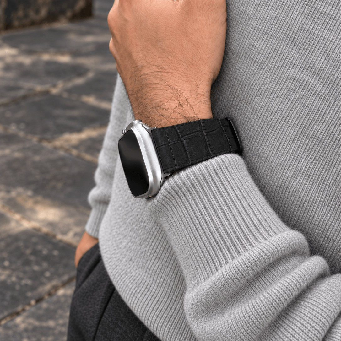 Dakkar Schwarz – 24 mm Apple Watch Ultra Lederarmband in Kroko-Optik an Handgelenk eines Mannes in grauem Pullover.