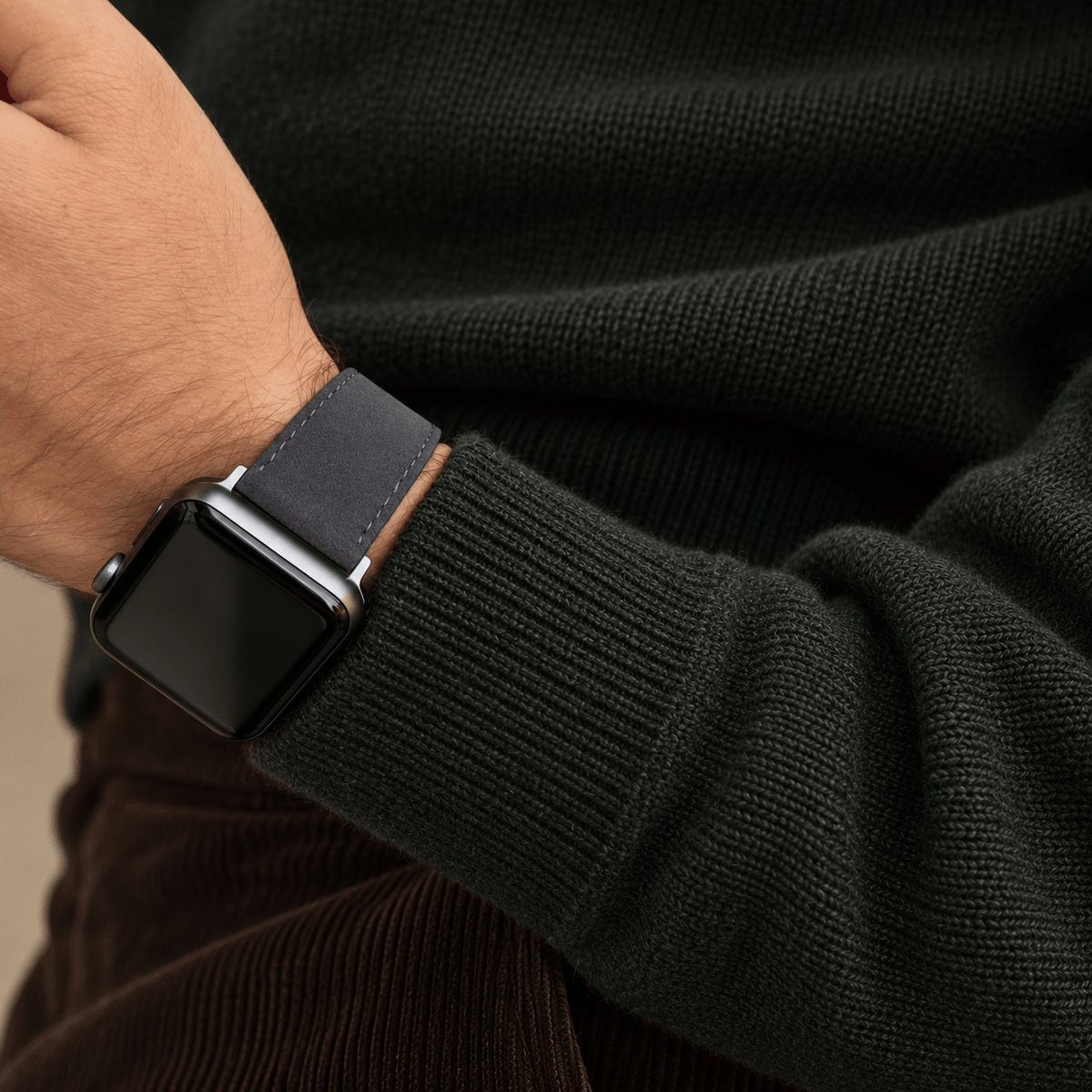 Alcantara – Apple Watch Armband in Dunkelgrau an Hand mit grauem Pullover kombiniert.