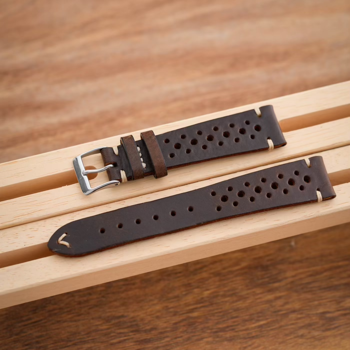 Uhrenarmband Racing in dunklem Leder mit markanten Löchern, elegant auf einem Holzuntergrund präsentiert.