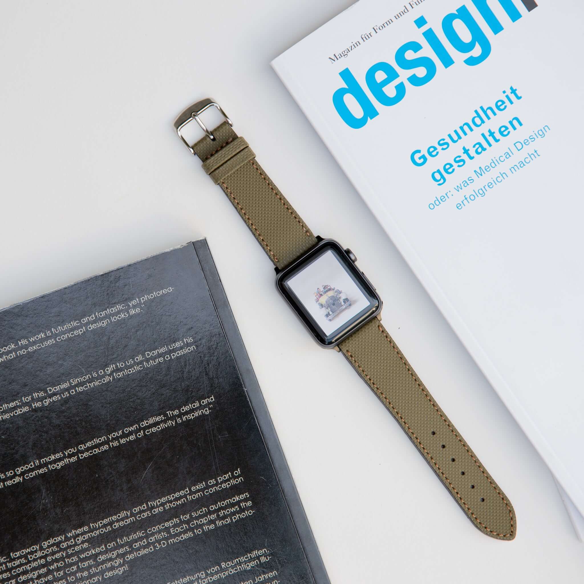 Stylisches apple watch lederarmband wasserfest in olivgrün, getragen an einer Apple Watch, neben Designmagazinen platziert.