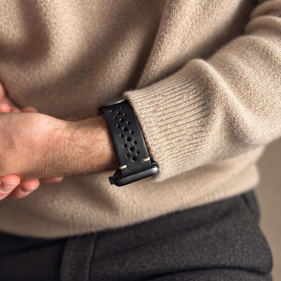Rallye Lederband für Apple Watch - Schwarz am Handgelenk eines Mannes mit beigem Pullover.