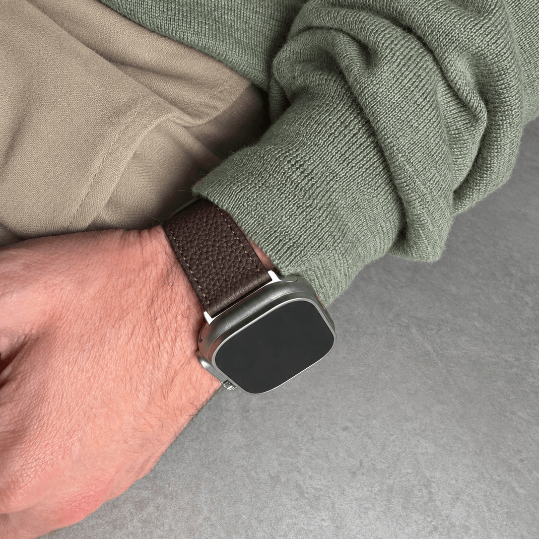 Dunkelbraunes Lederarmband für Apple Watch aus Togoleder, tragend an hand mit grünem Oberteil.