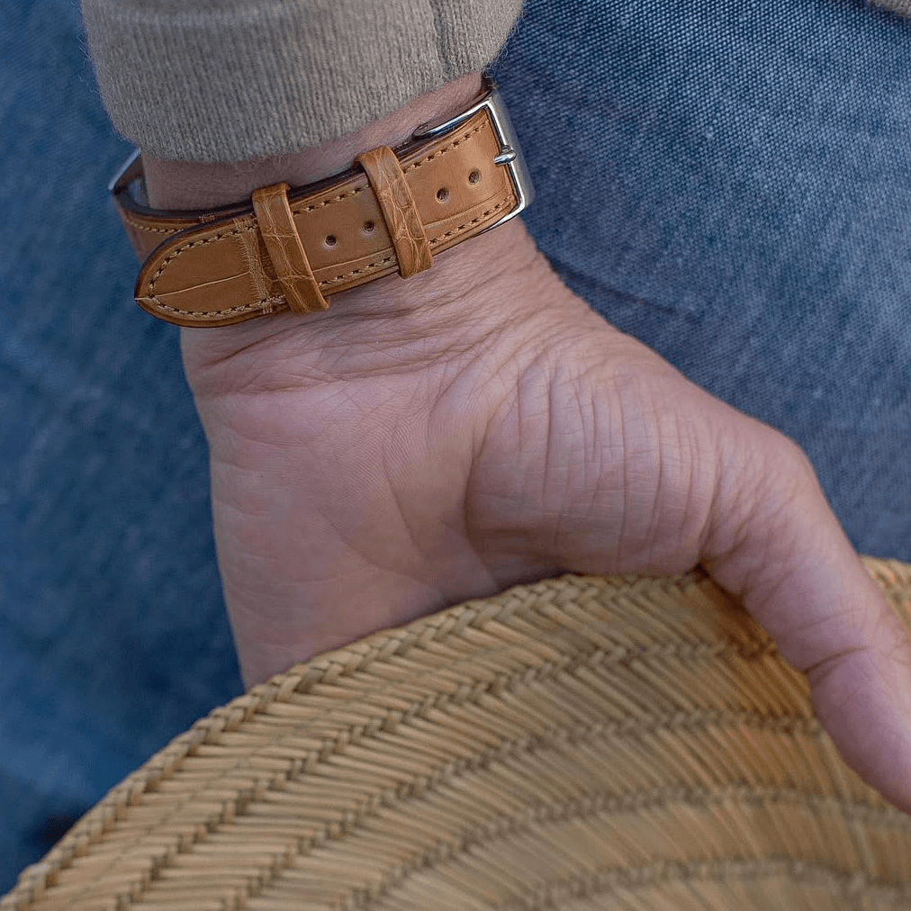 Nahaufnahme von Louisiana Alligator Uhrenarmband-Full Cut in Cognac auf einem Handgelenk, kombiniert mit Strohhut.