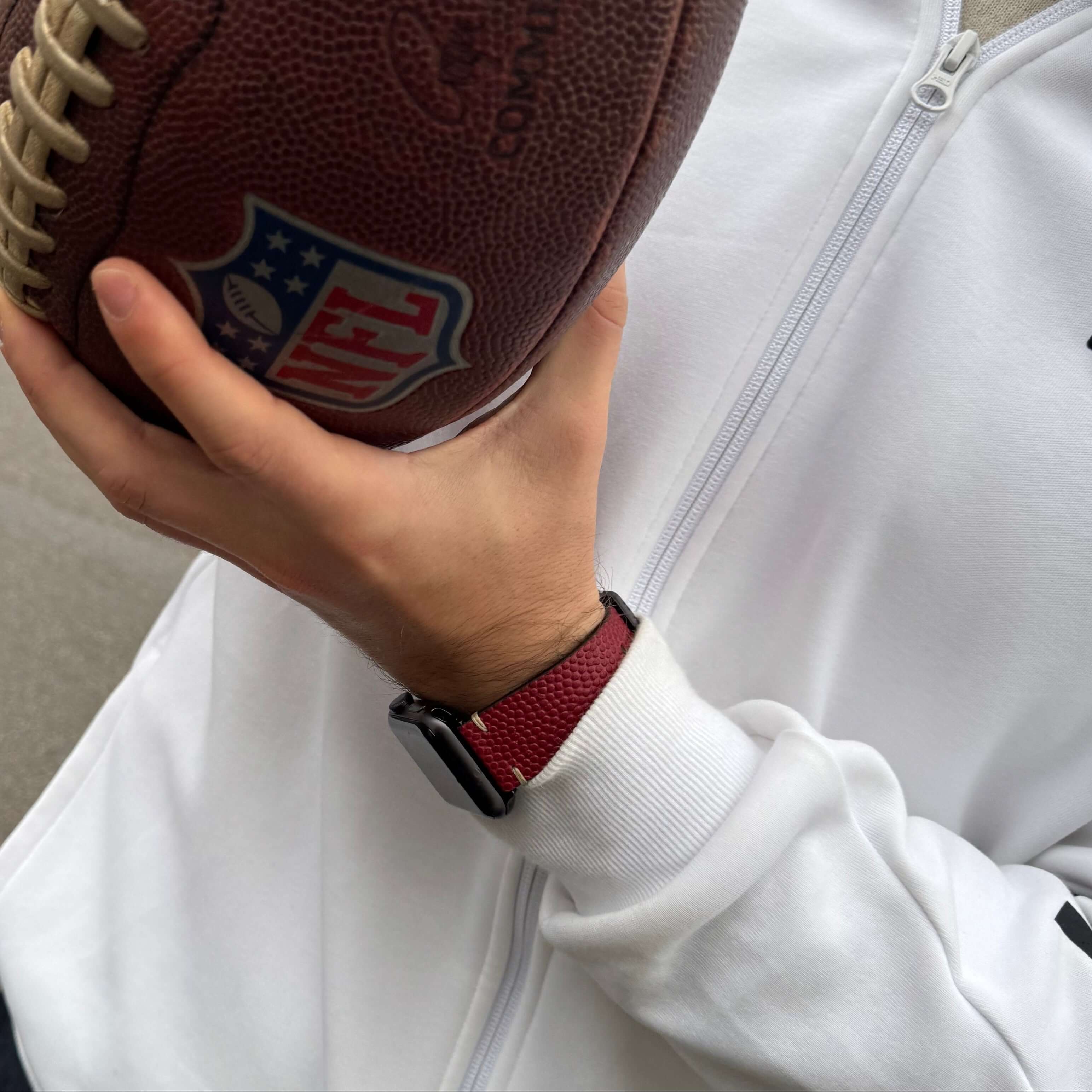 Wilson – Handgefertigt aus original Horween Footballleder Armband an Apple Watch neben NFL-Football in der Hand.