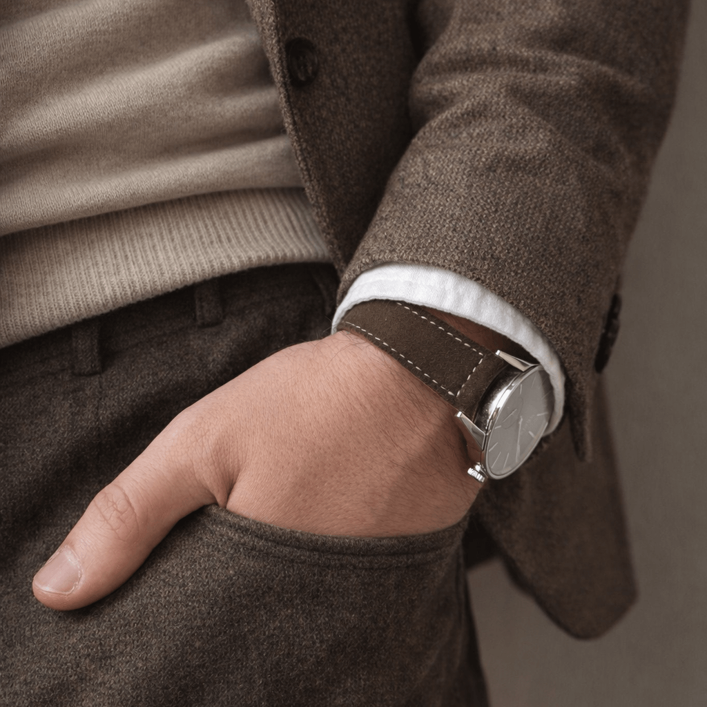 Alpen – Lederhosenband aus altsämisch gegerbtem Hirschleder, getragen am Handgelenk über einem braunen Tweed-Outfit