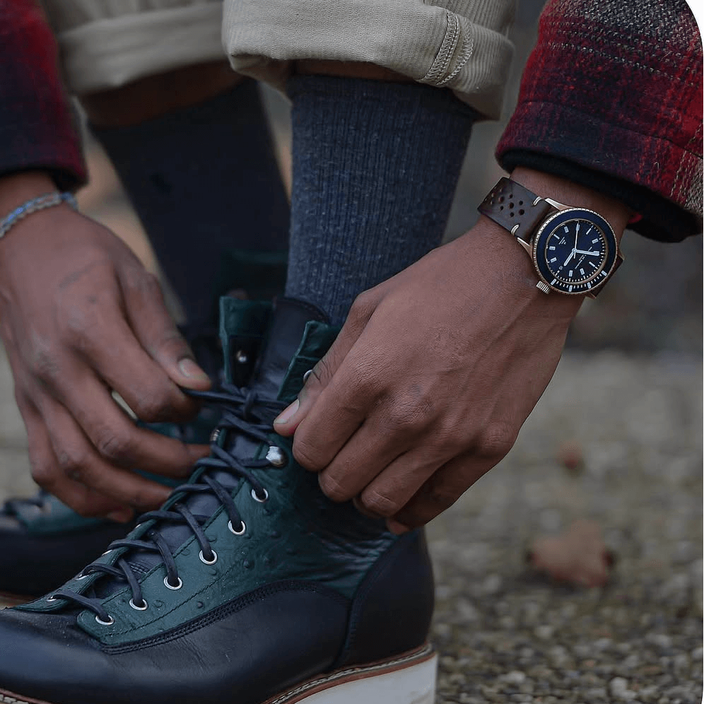 Person trägt Hunter Leder Uhrenarmband Racing, bindet Schuhe auf natürlichem Hintergrund, sportliche Eleganz und traditionelle Handwerkskunst.