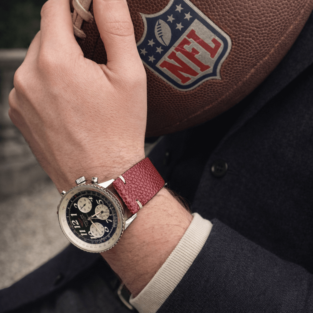 Touchdown – Uhrenarmband handgefertigt aus original Horween Footballleder an Breitling Navytimer, gehalten mit NFL-Ball.