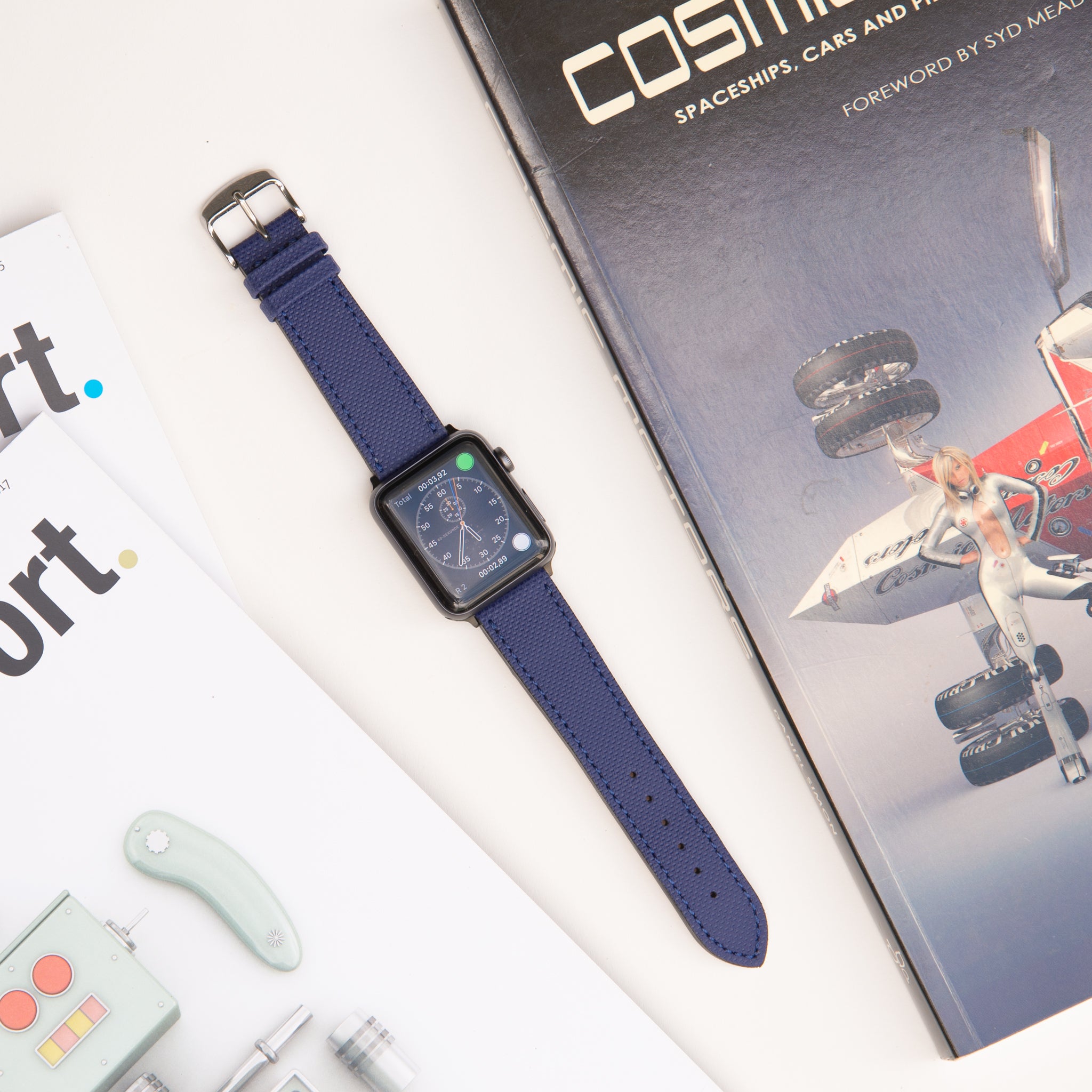 Sportliches apple watch lederarmband wasserfest in blau, sichtbar an einer Apple Watch, neben Zeitschriften und einem Designbuch.