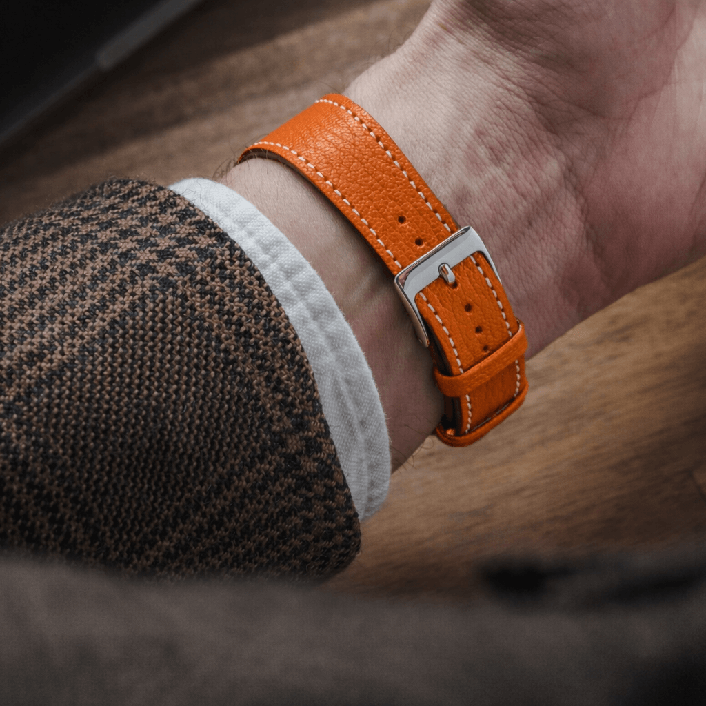 Biarritz – Uhrenarmband aus französischem Ziegenleder in Orange am Handgelenk eines Mannes mit brauner Jacke, Nahaufnahme.